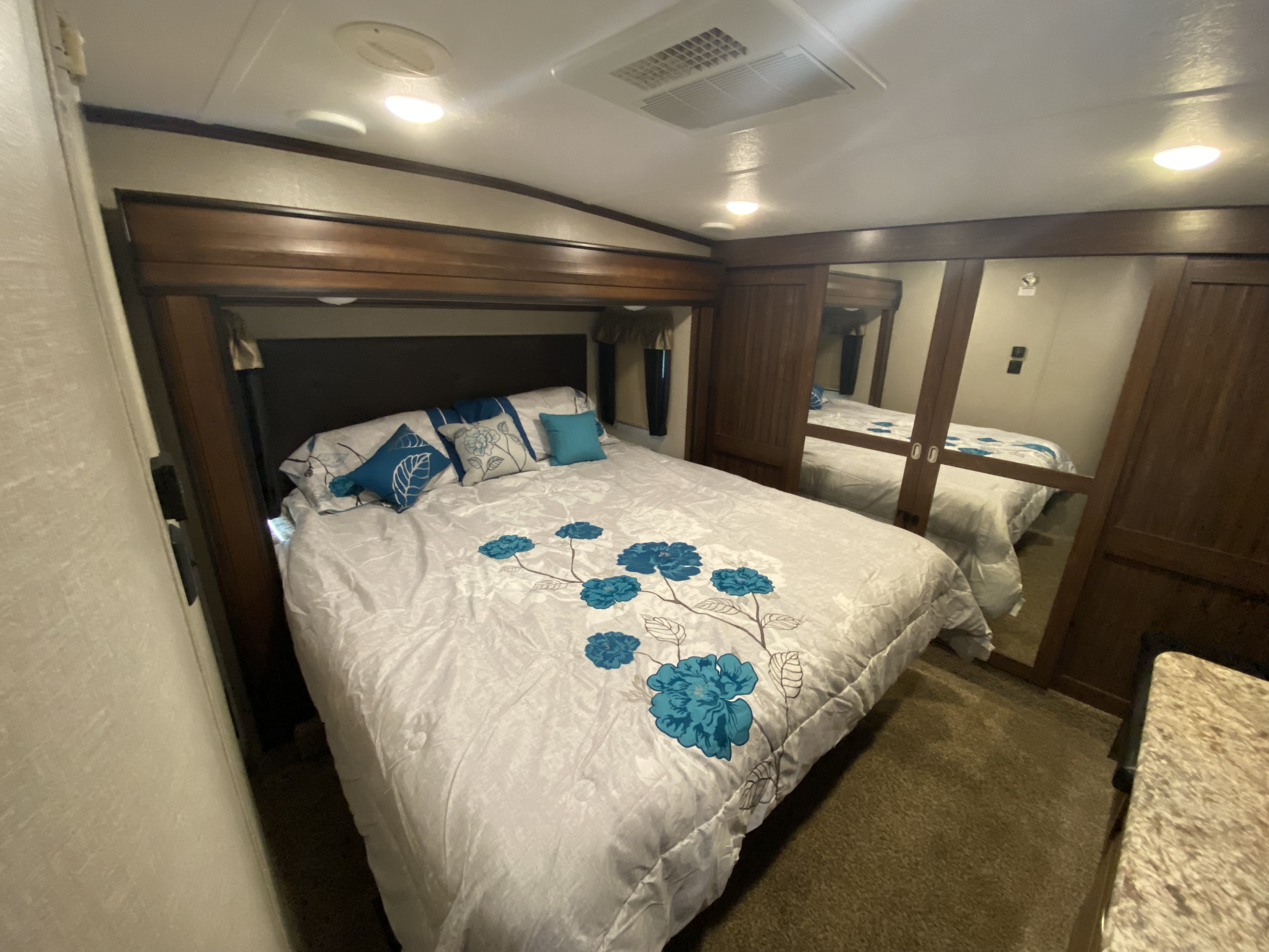 RV rental bedroom showcasing a bed with blue floral bedding, mirrored closet doors, and overhead lighting.. Keystone RV Montana High Country 2017