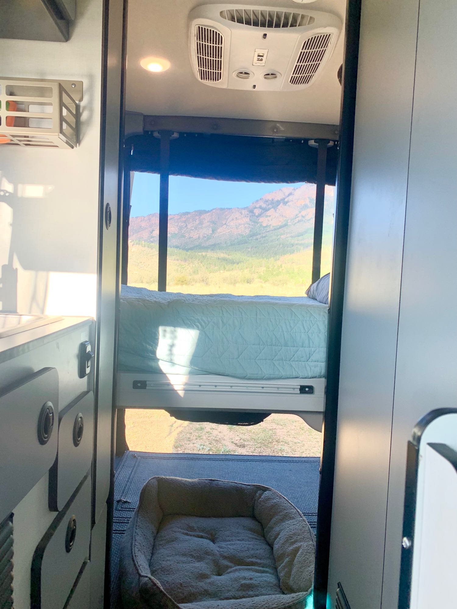 Cozy RV rental interior: a bed and dog bed overlook a stunning mountain vista through the rear window. Perfect for adventure.. Winnebago Revel 2021