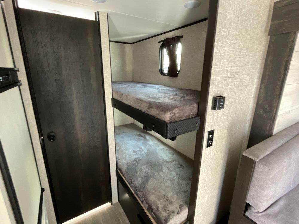 RV rental interior: stacked bunk beds, a dark door, a window, and wall-mounted power outlets.. Jayco Jay Flight SLX Baja Edition 2023