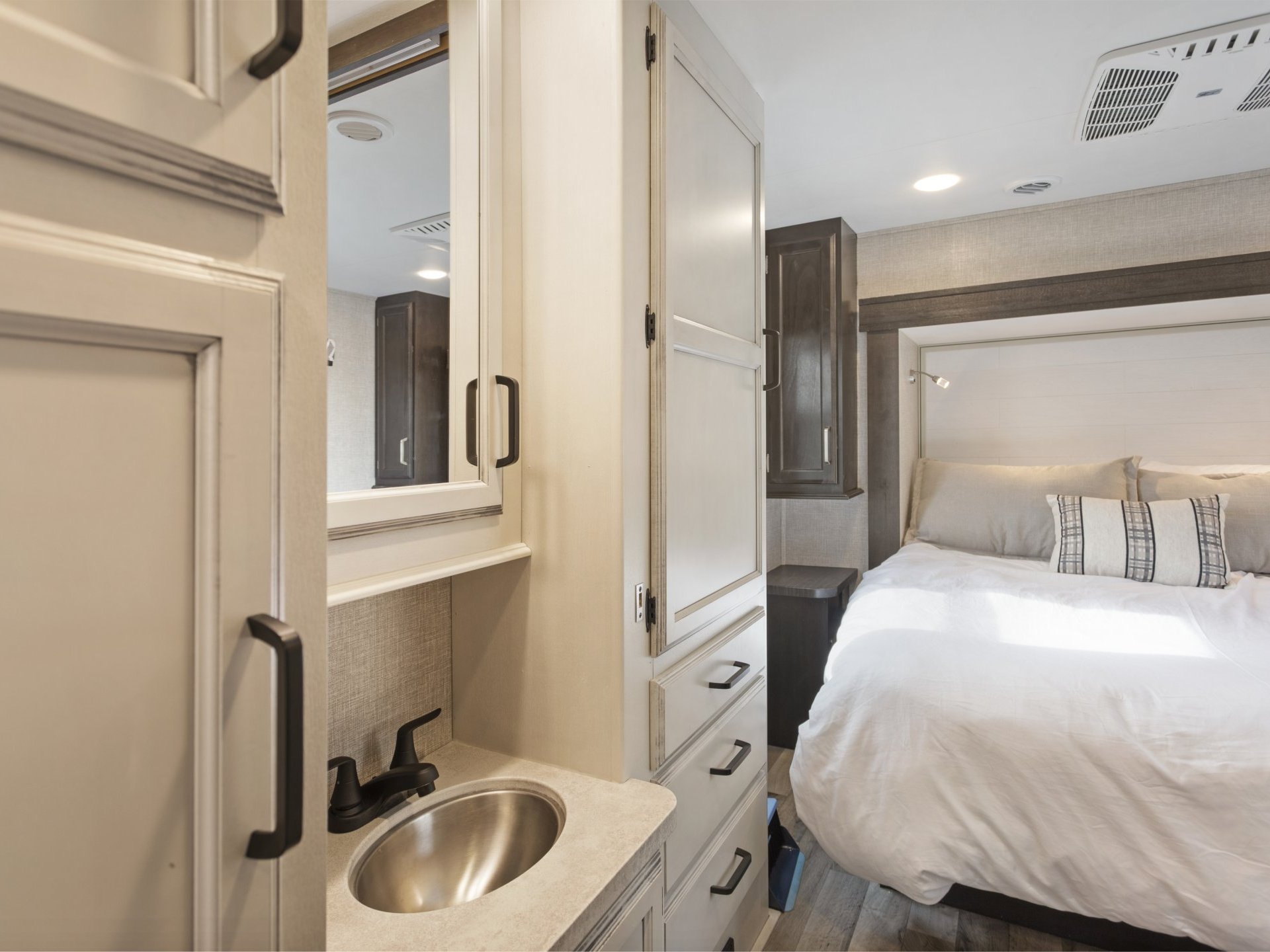 Inside a modern RV rental, showing a cozy bedroom with bed and an adjacent compact bathroom vanity with sink.. Entegra Coach Odyssey 2021