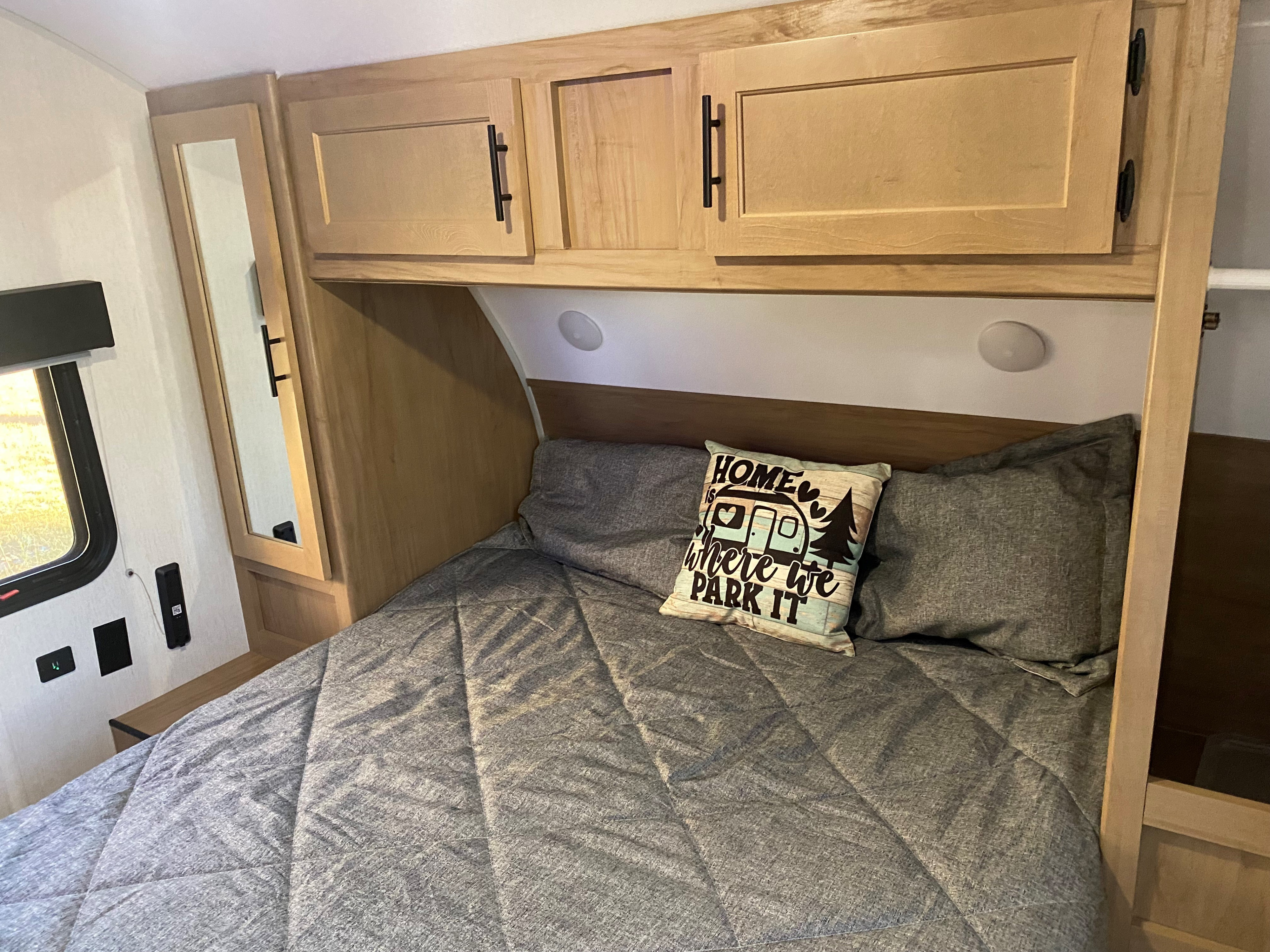 Cozy RV rental bedroom with a grey bed, light wood overhead cabinets, & a "Home is where we PARK IT" pillow.. Forest River Cherokee Grey Wolf 2023