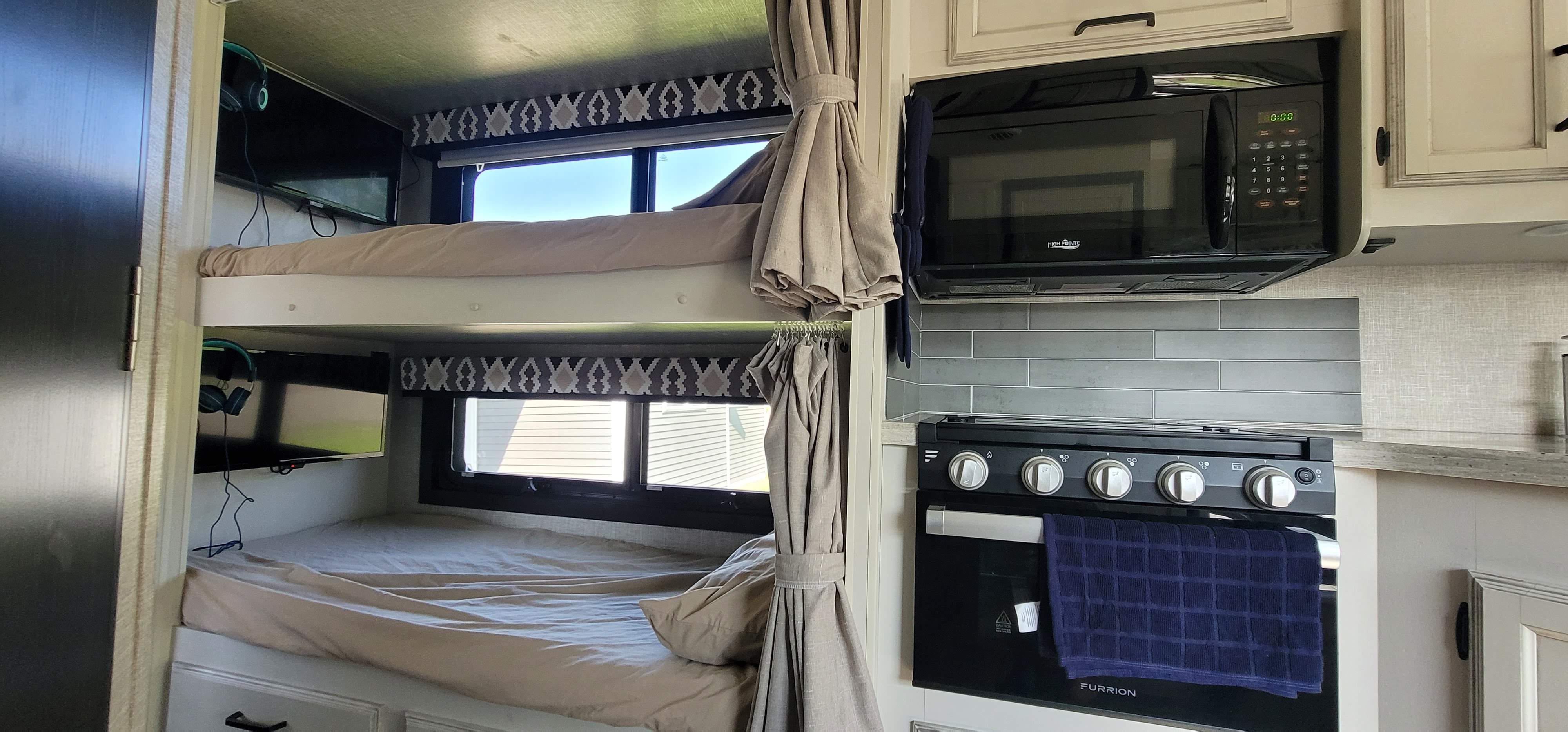 Spacious RV rental interior featuring cozy bunk beds with TVs, and a functional kitchen area with microwave and oven.. Jayco Alante 2022