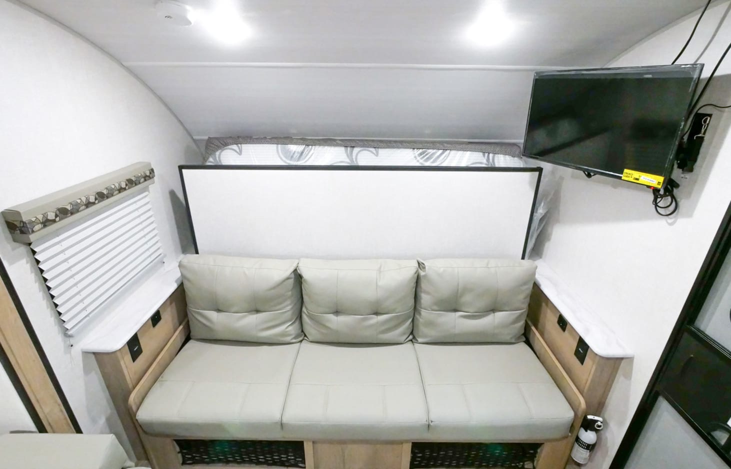 Modern RV rental interior with a light-colored convertible sofa, wall-mounted TV, and window blinds.. R-Pod R-Pod Trailer 2021