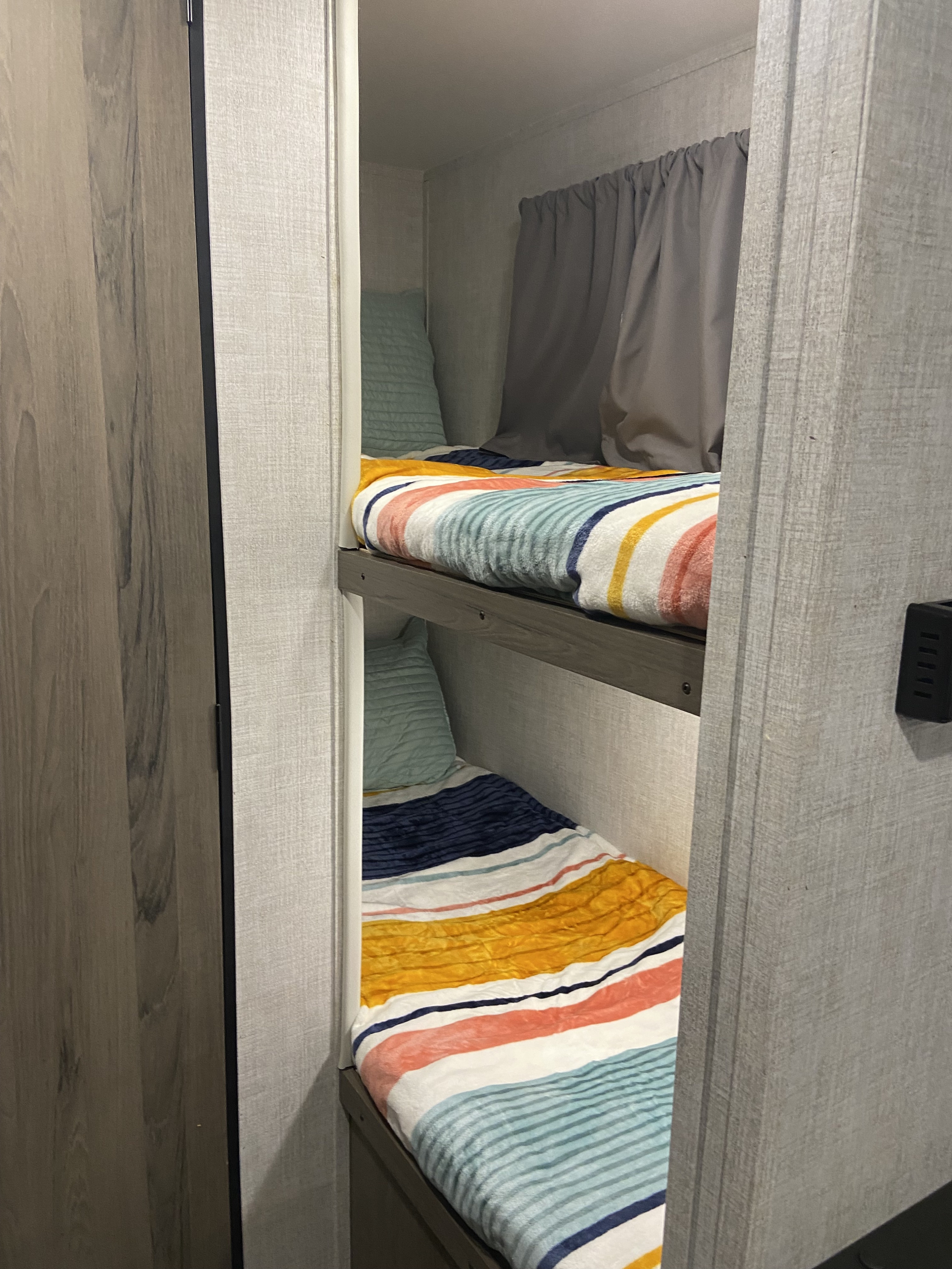 Cozy RV rental bunk beds with colorful bedding, featuring grey privacy curtains, inside a comfortable camper.. Gulf Stream Enlighten 2021