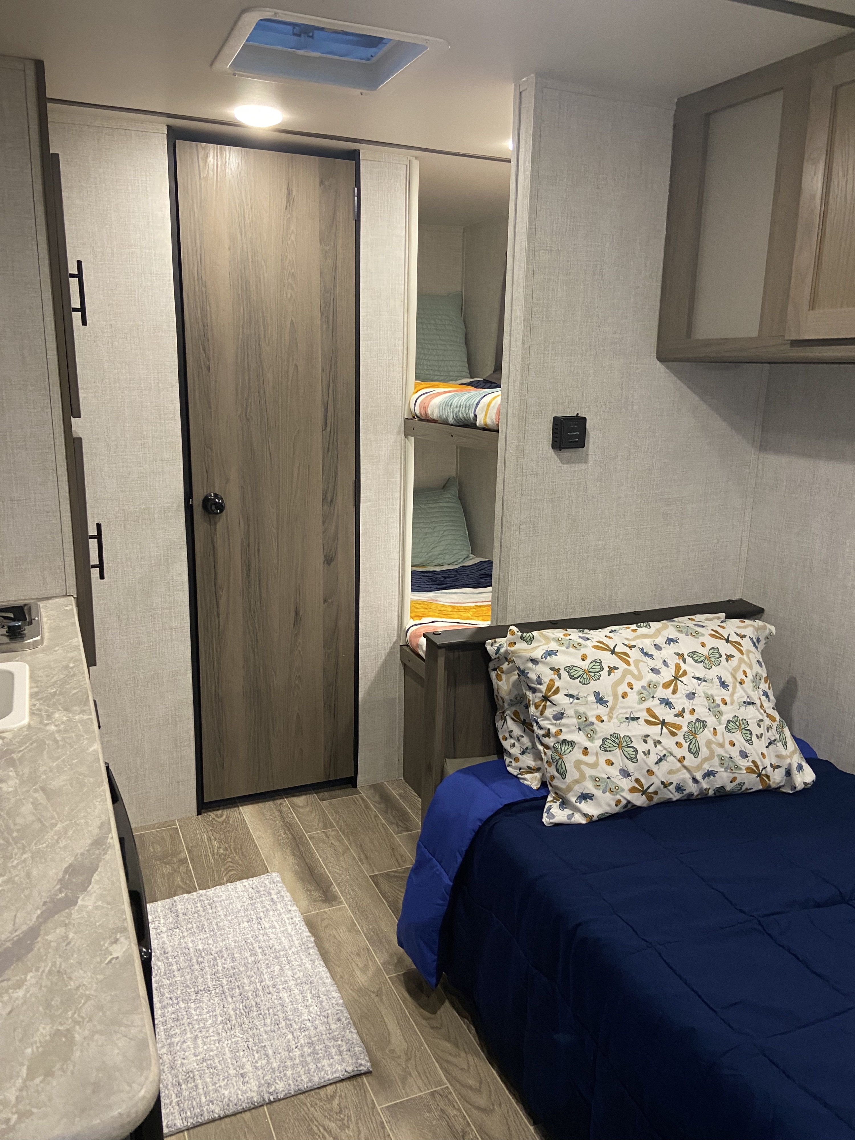 Cozy RV rental interior featuring a bedroom, bunk beds, and partial kitchen. Ideal for family adventures.. Gulf Stream Enlighten 2021