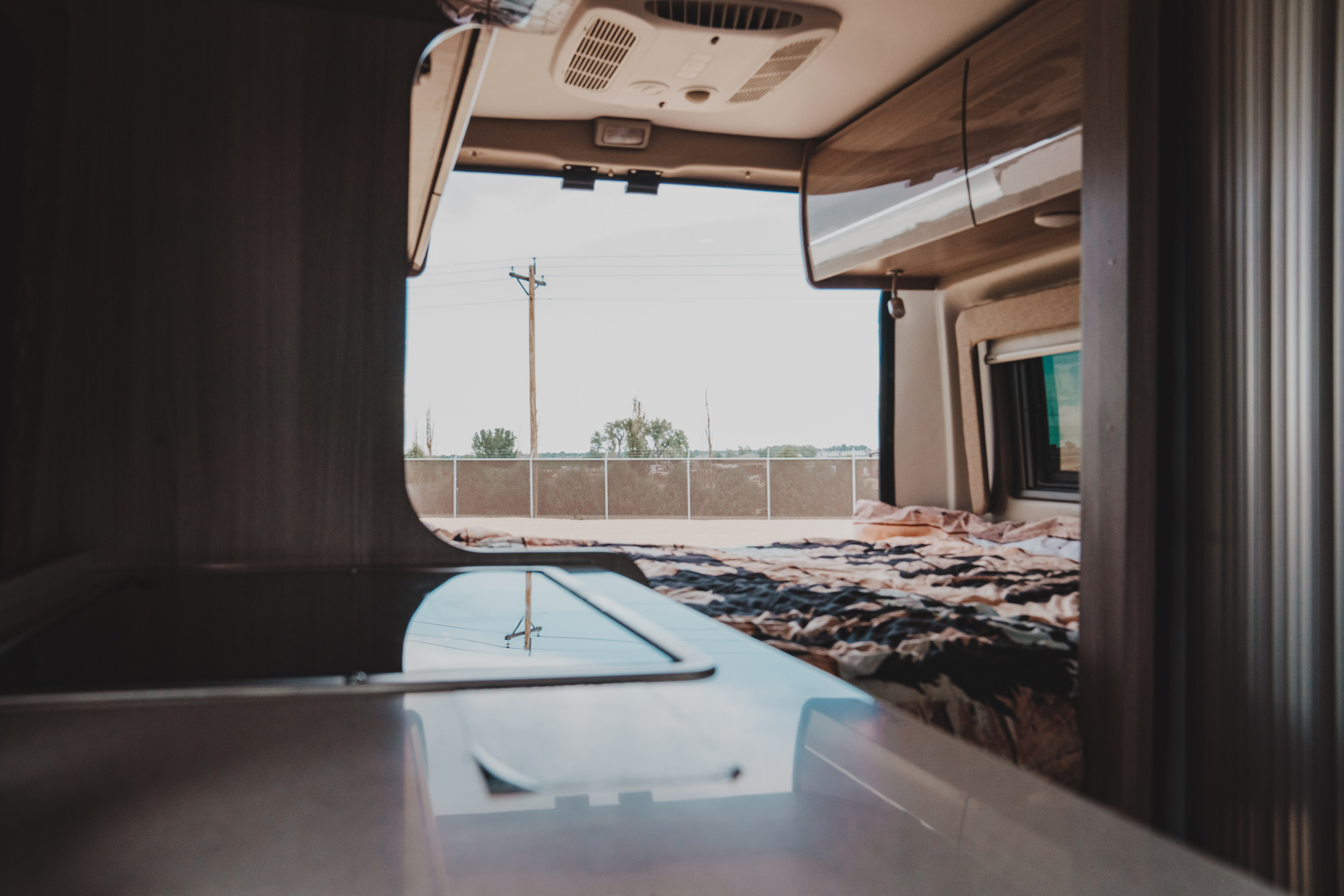 RV rental interior: cozy bed, overhead cabinets, and an expansive view of the outdoors reflected on the counter.. Thor Motor Coach sequence 2021