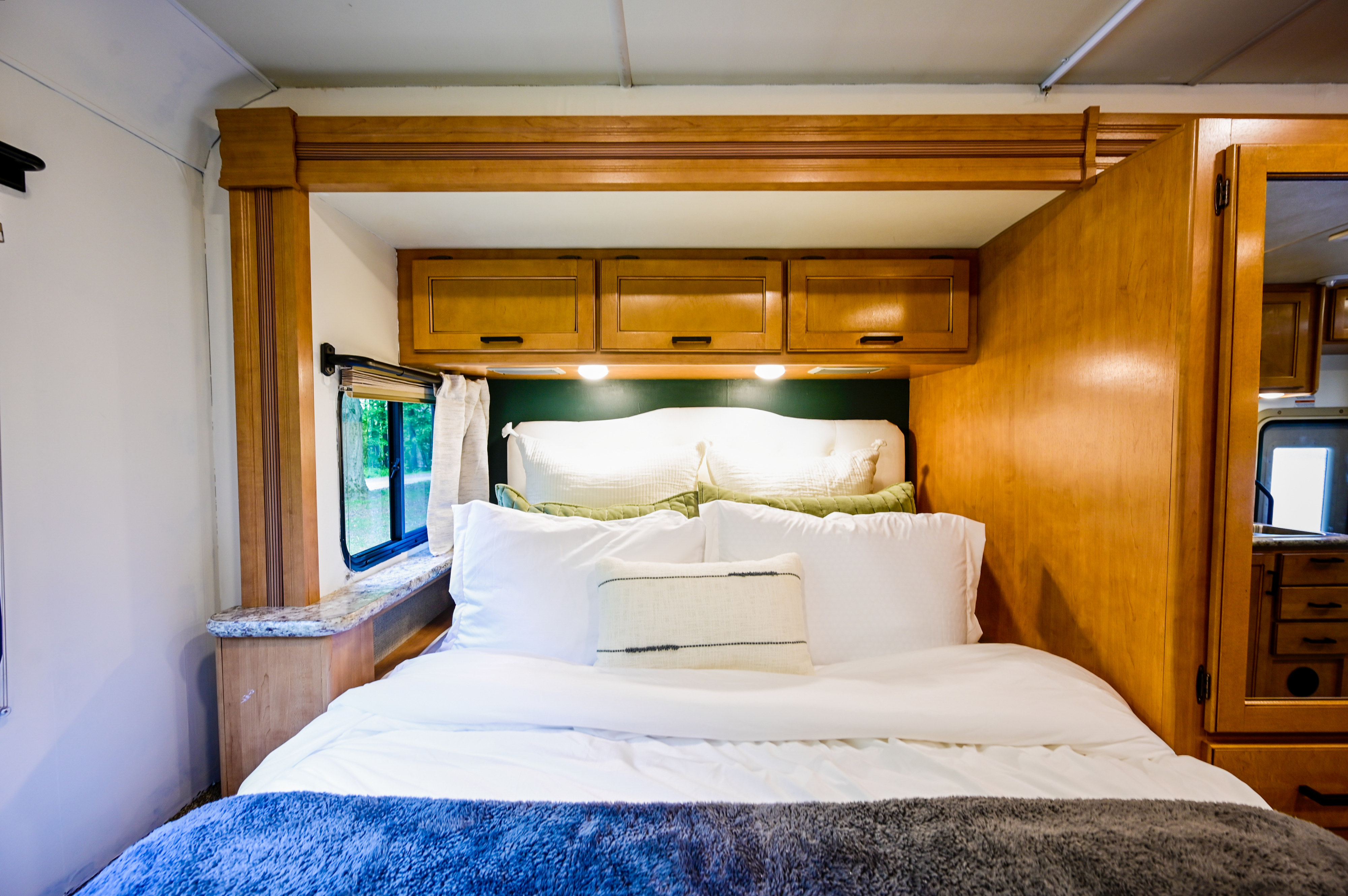 Cozy RV rental bedroom with white bedding, plush pillows, wooden cabinetry, and a window for natural light.. Thor Chateau 2017