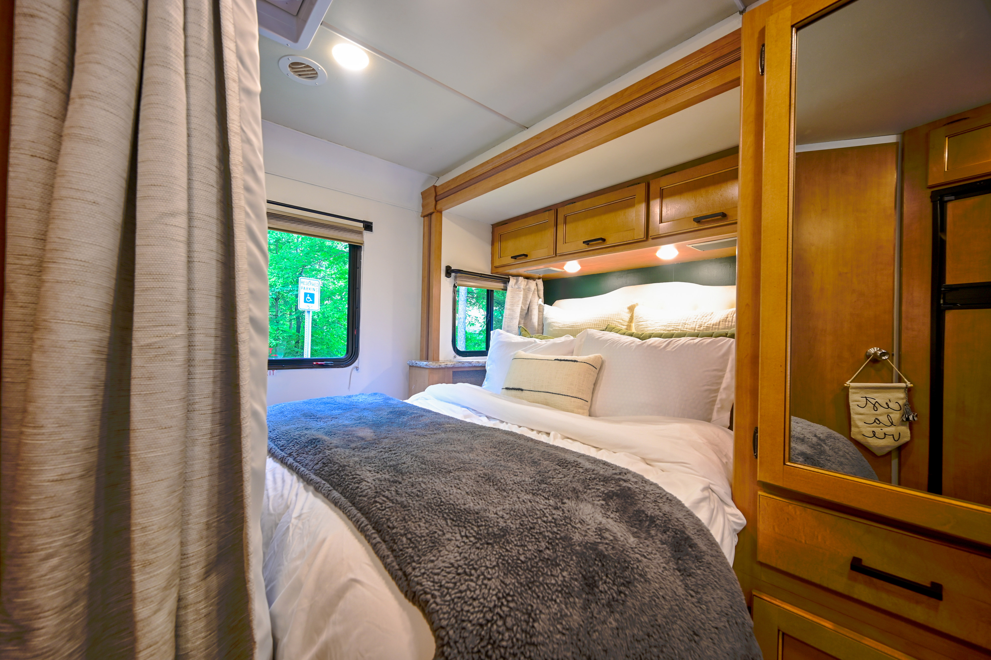 Comfortable RV rental bedroom interior features a cozy bed, overhead storage, and a scenic window view of green trees.. Thor Chateau 2017