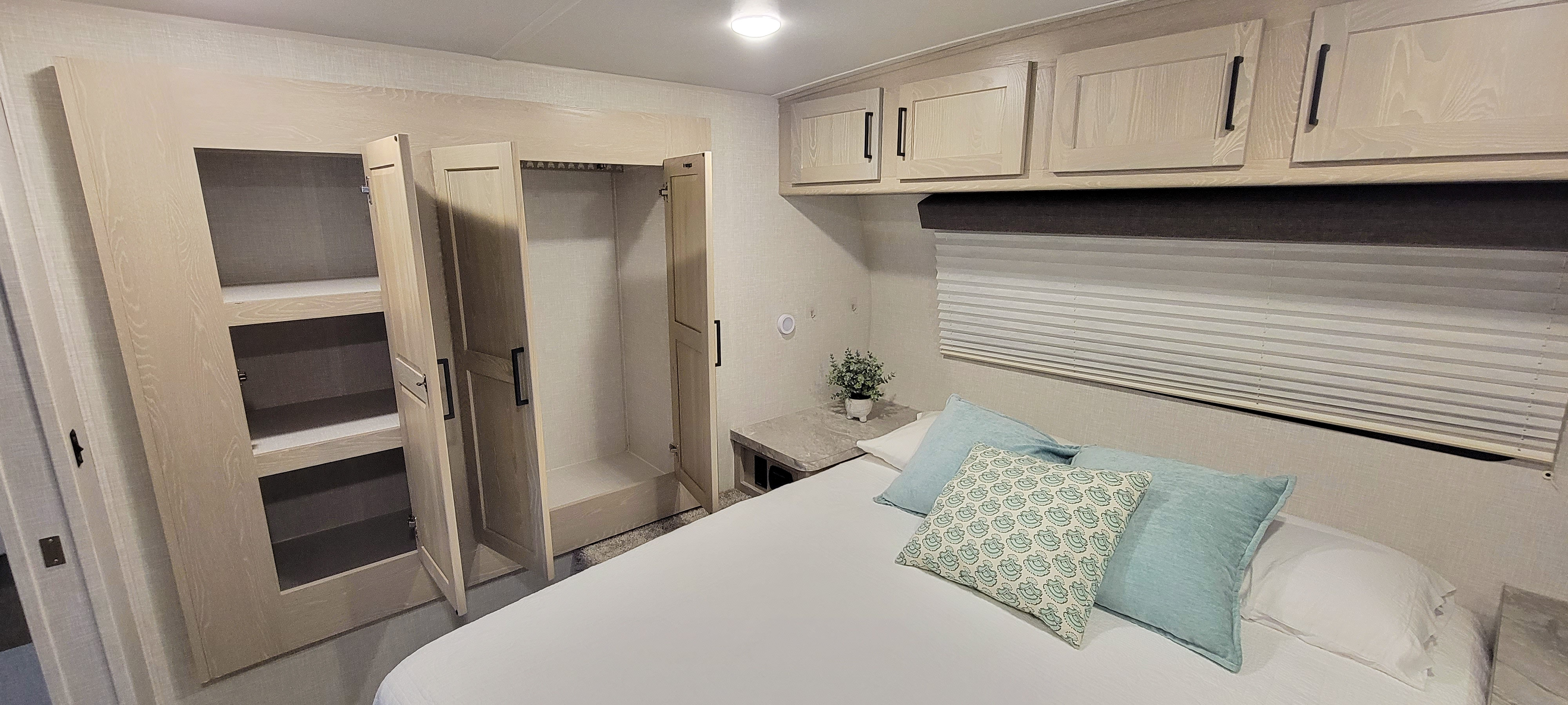Modern RV rental bedroom. Features a comfy bed, overhead cabinets, and spacious, open closets with shelves.. Forest River Rockwood Mini Lite 2021