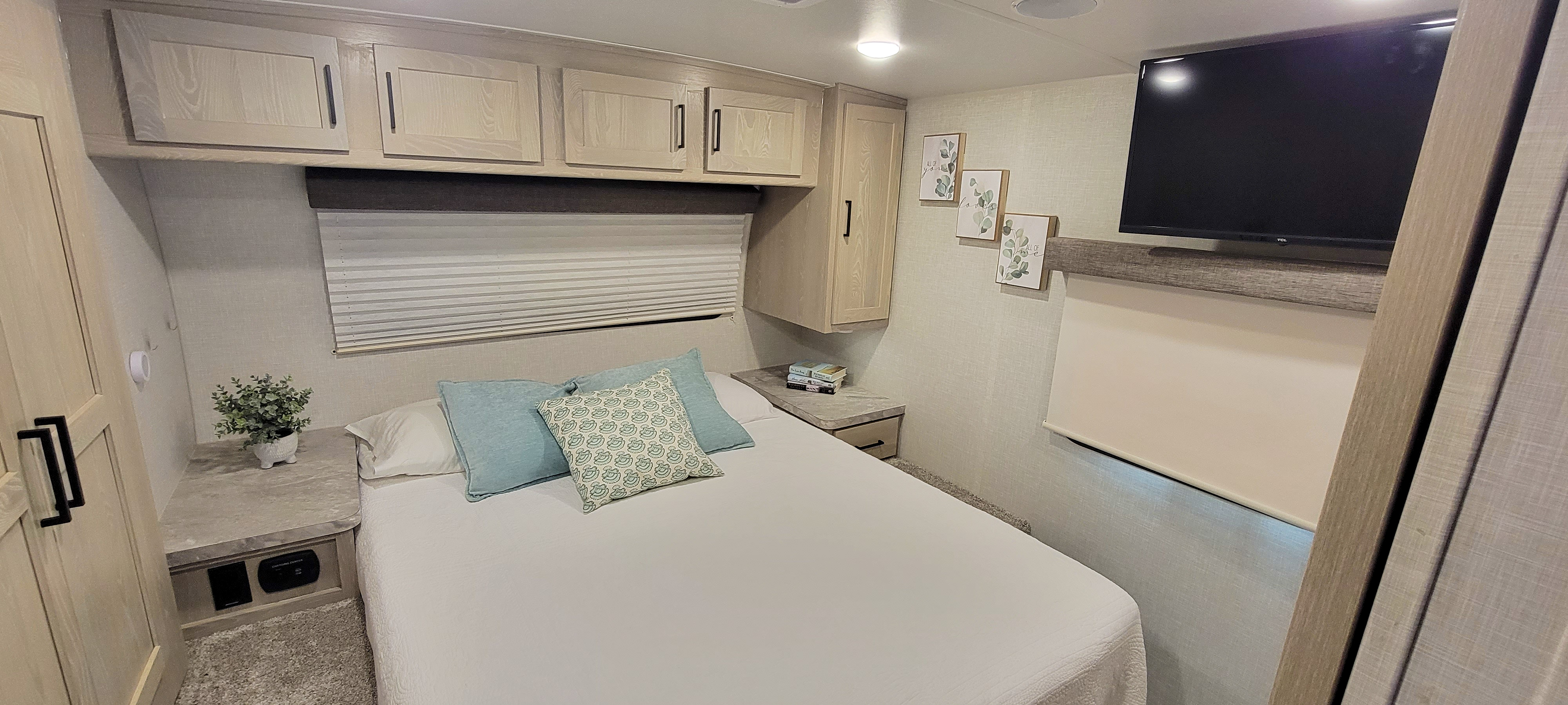 Cozy RV rental bedroom with a comfortable bed, overhead storage, window blinds, and a TV. Ideal for travel adventures.. Forest River Rockwood Mini Lite 2021