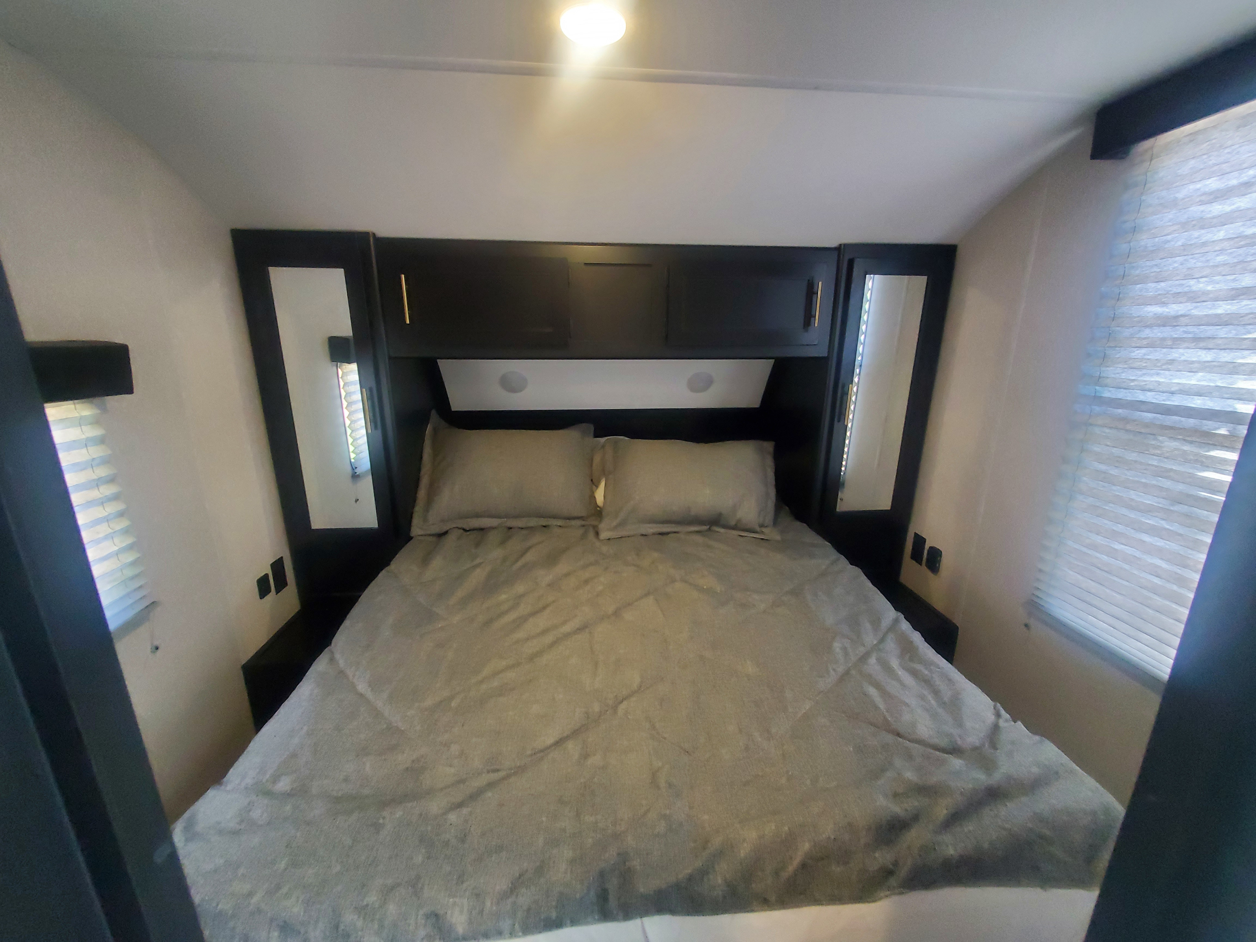 RV rental bedroom: gray bed, overhead cabinets, side mirrors, and windows with blinds. A compact and functional space.. Forest River Cherokee Grey Wolf 2022