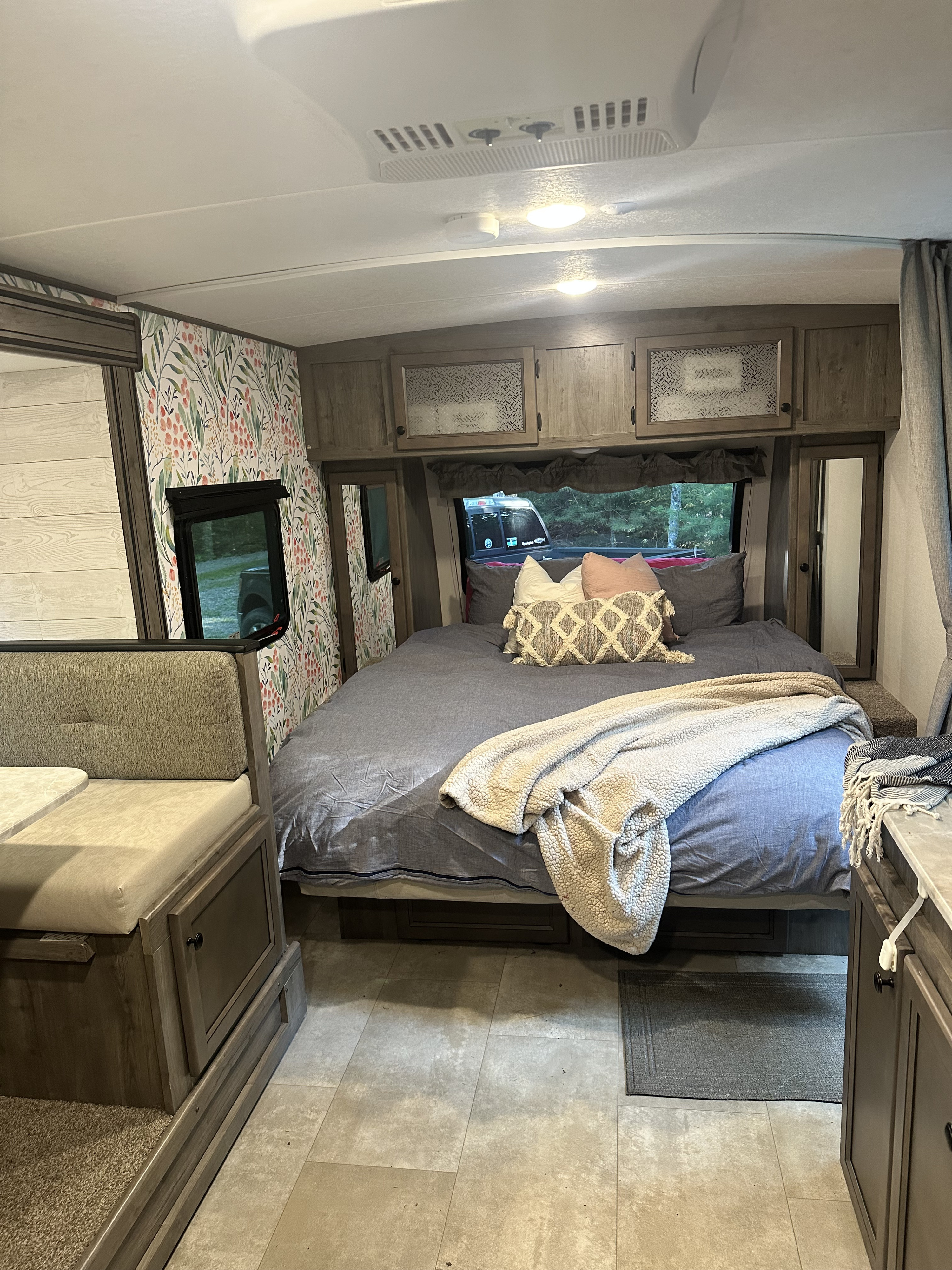 Cozy RV rental interior showcasing a bedroom with a large bed, pillows, and blanket, plus a dinette and floral wallpaper.. Coachmen Apex Nano 2021