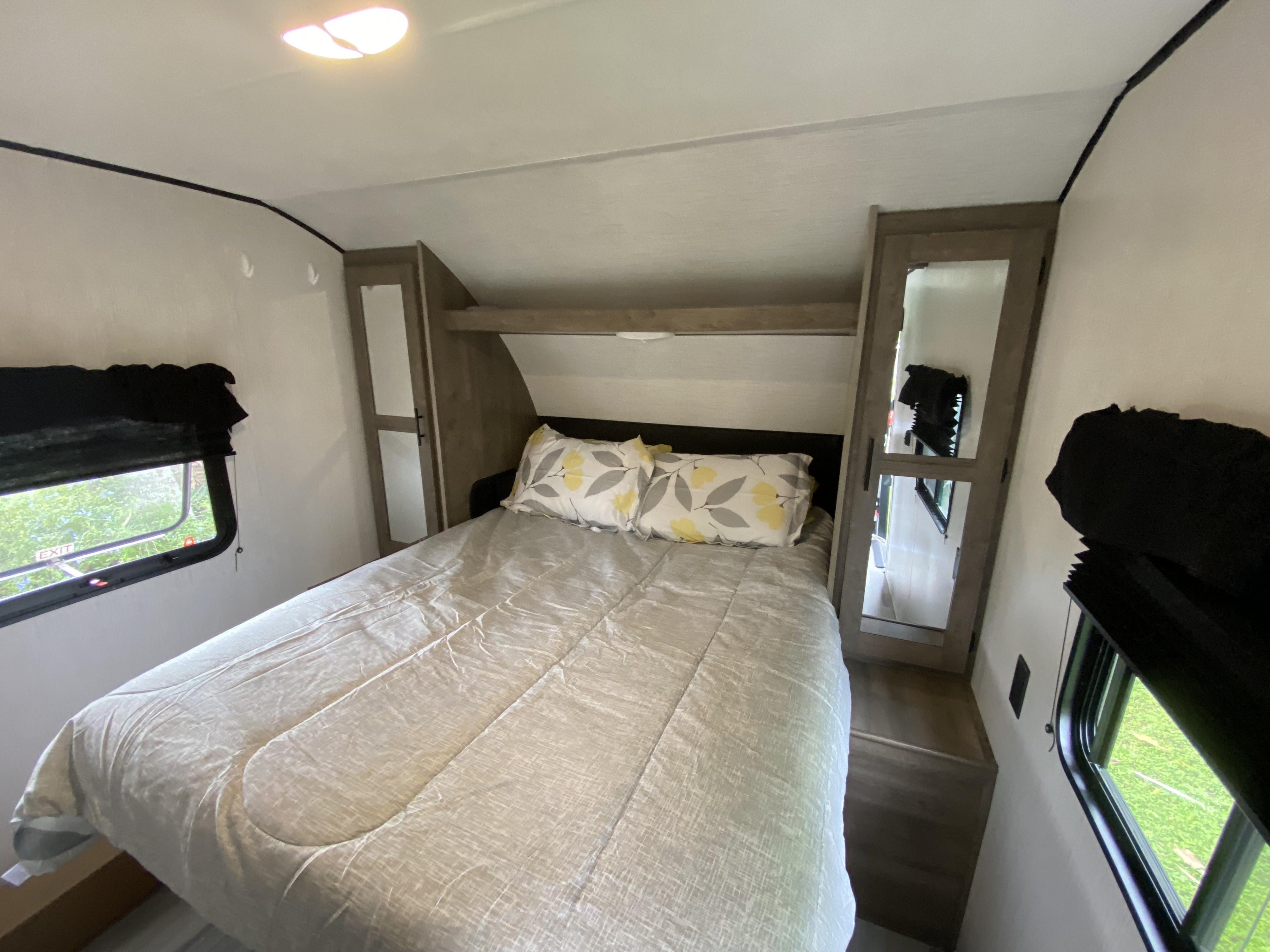 Cozy RV rental bedroom featuring a comfy bed with patterned pillows, overhead storage, and two windows for natural light.. Heartland RVs Pioneer 2021