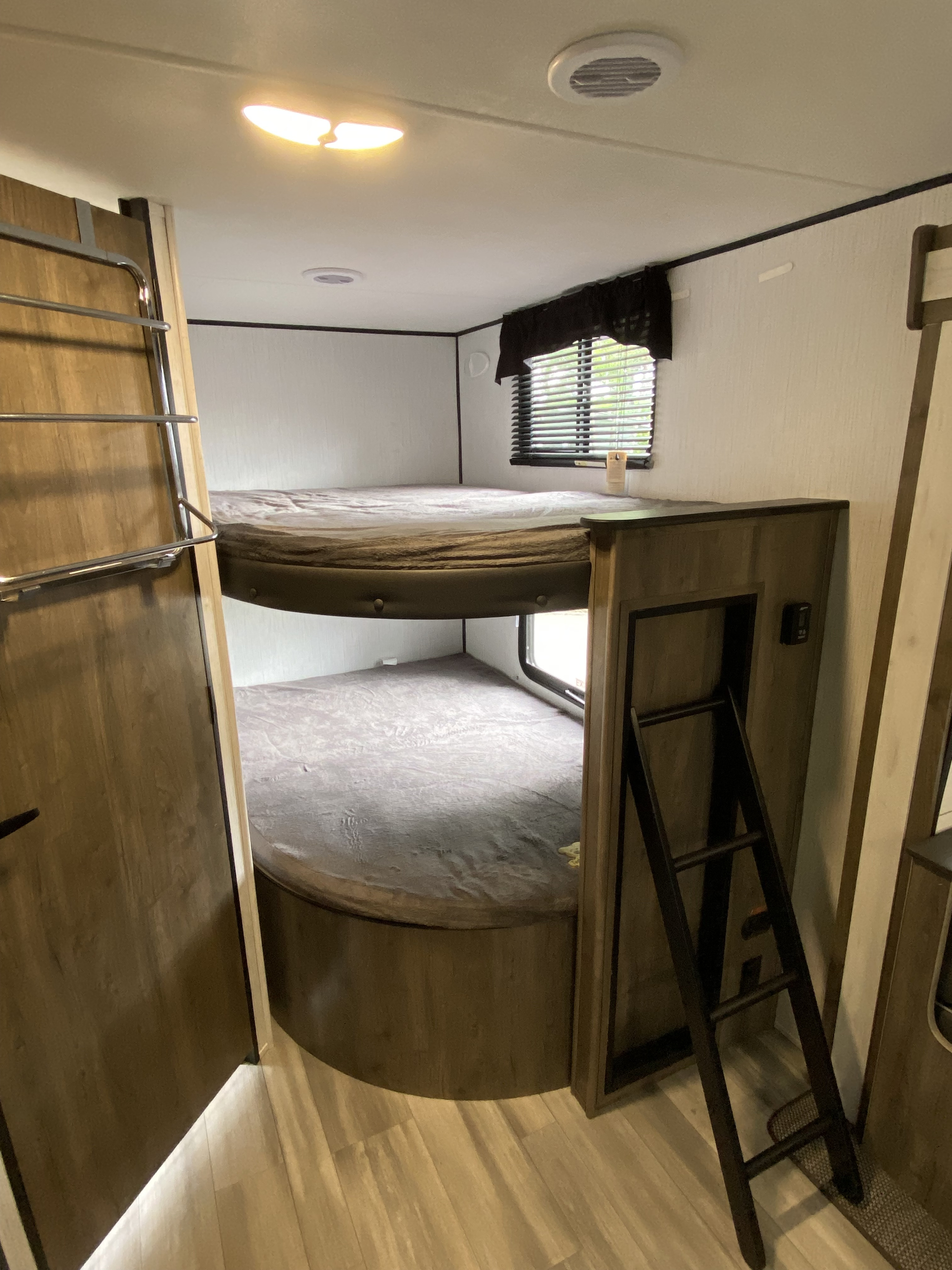 Cozy RV rental bunk beds, perfect for family adventures. Upper bunk has a window, with a ladder nearby.. Heartland RVs Pioneer 2021