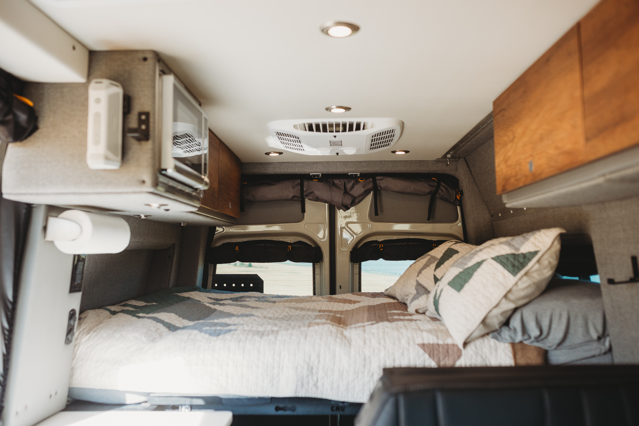 Interior of an RV rental camper van, featuring a cozy bed, microwave, and ceiling AC. Perfect for travel.. Storyteller Overland Storyteller Overland Class B 2023