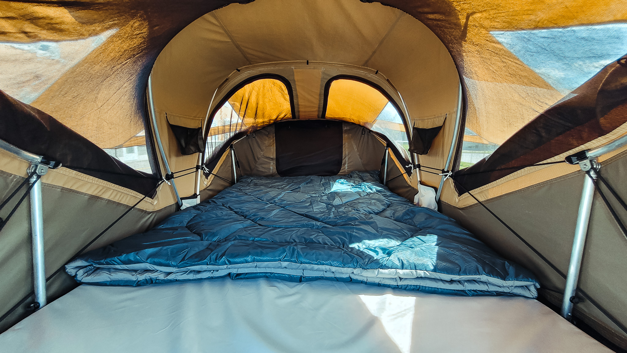 Step inside this RV rental's comfortable rooftop tent. A blue sleeping bag is folded on the white bed, ready for your trip.. Chevrolet Other 2023