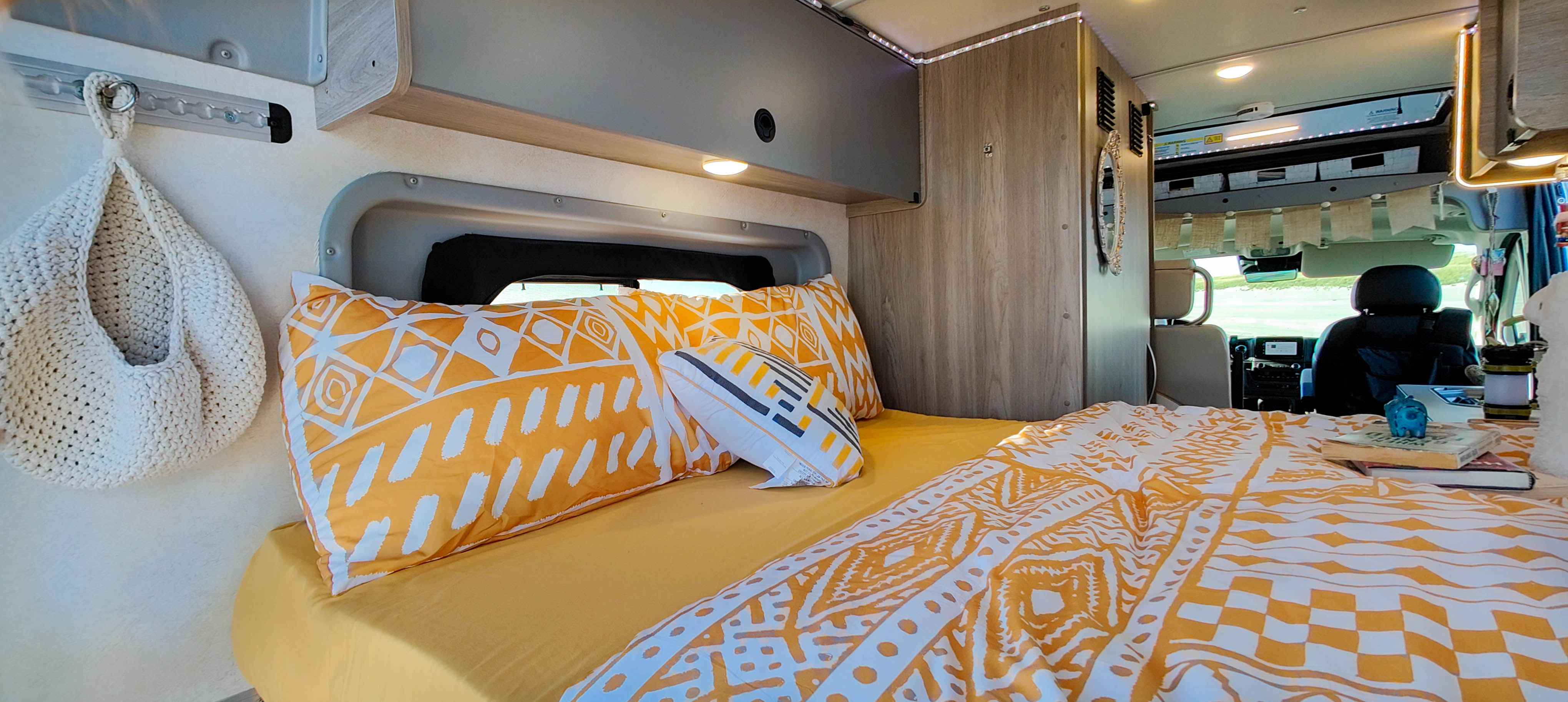 Comfortable RV rental interior with a cozy bed, vibrant yellow and white patterned bedding, overhead storage, and front cabin view.. Winnebago Solis 2023