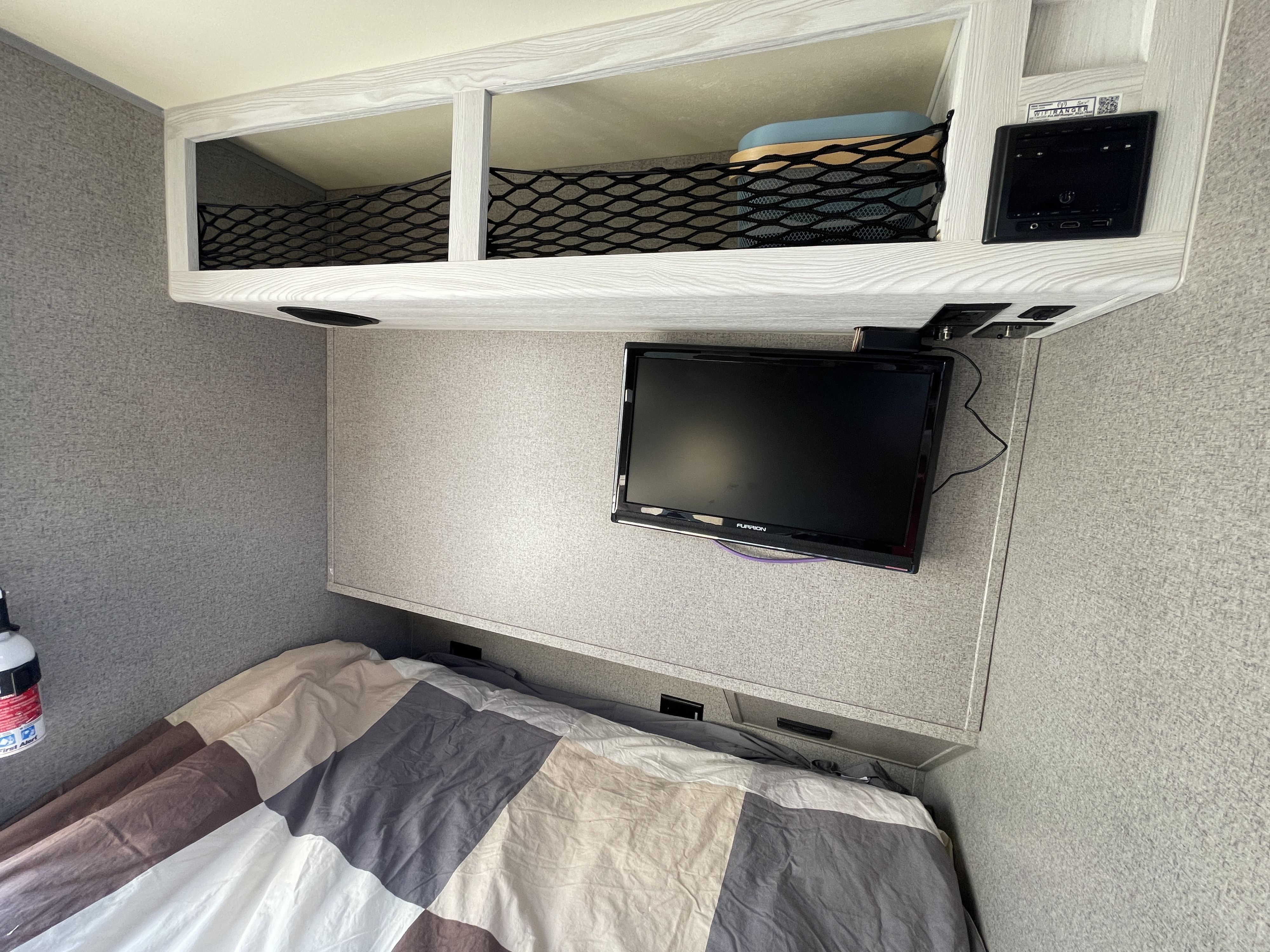 RV rental: Compact camper bedroom showing a bed, wall-mounted TV, overhead net storage, and a fire extinguisher.. Forest River Rockwood Geo Pro 2018