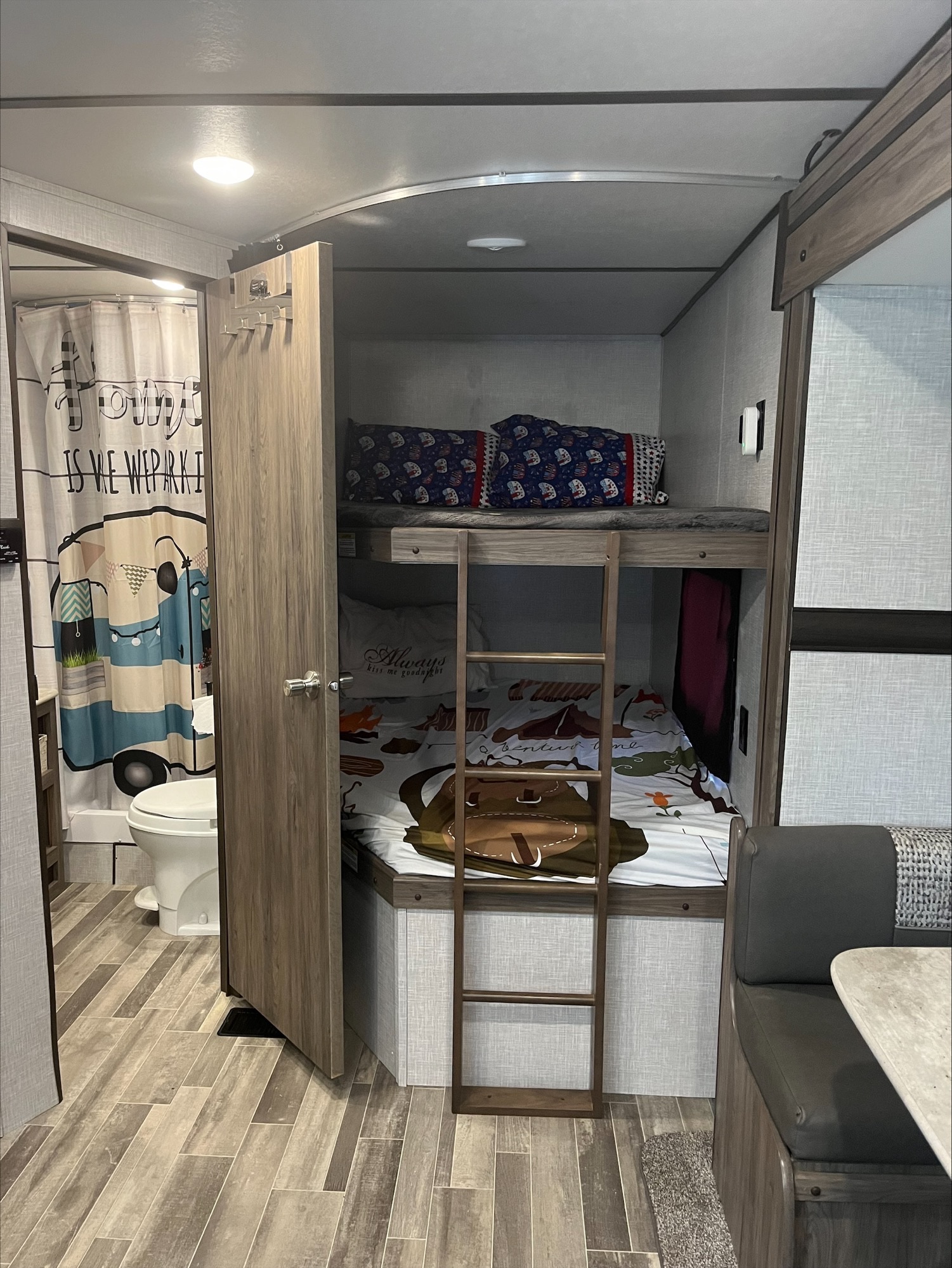 Explore a cozy RV rental interior: bunk beds, compact bathroom with camper shower curtain, and dining area on wood-look floors.. Crossroads RV Zinger Lite 2021