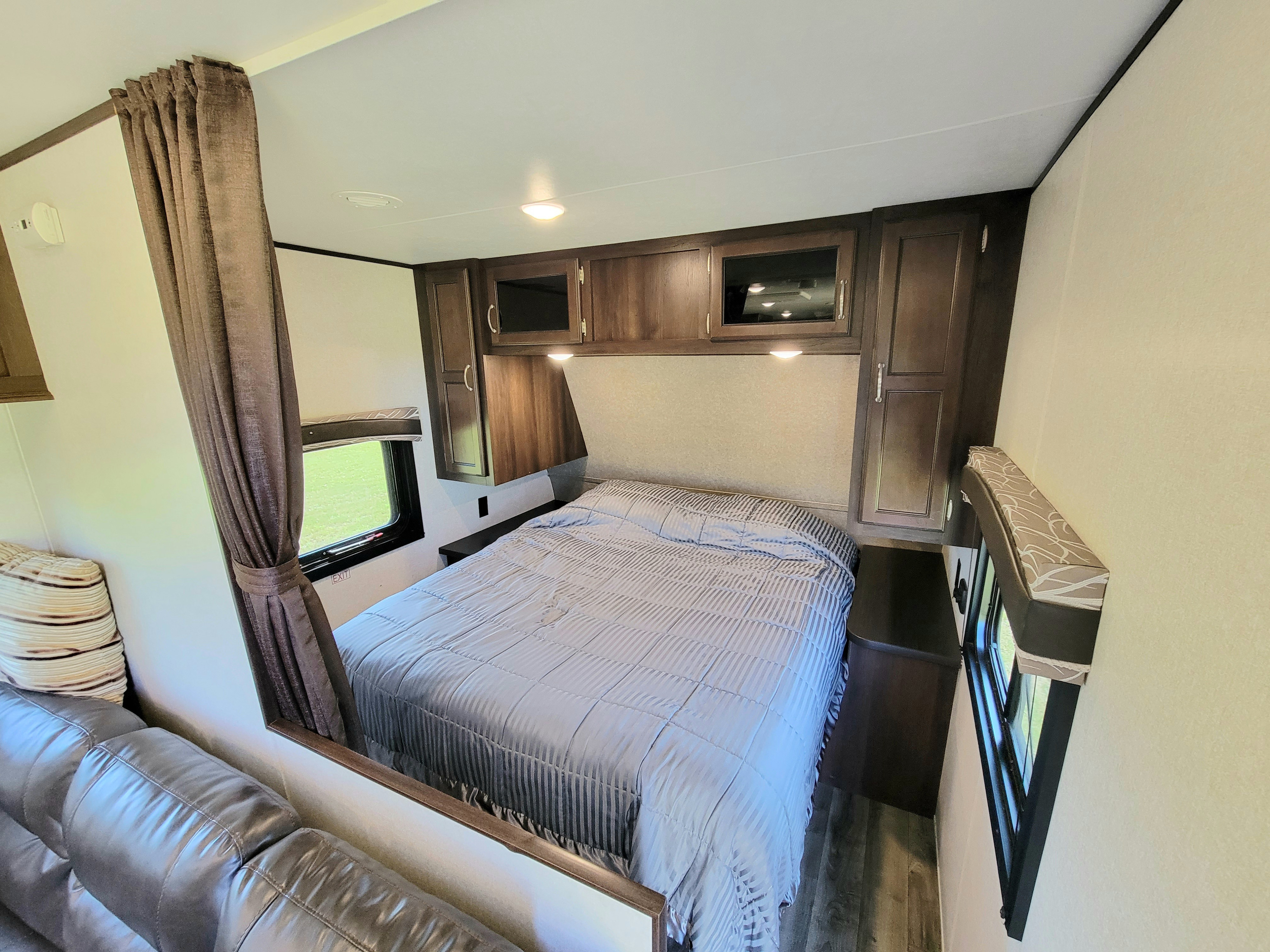 An inviting RV rental bedroom with a striped bed, overhead cabinets, and a curtained window. Perfect for comfortable road trips.. Jayco Jay Flight 2018
