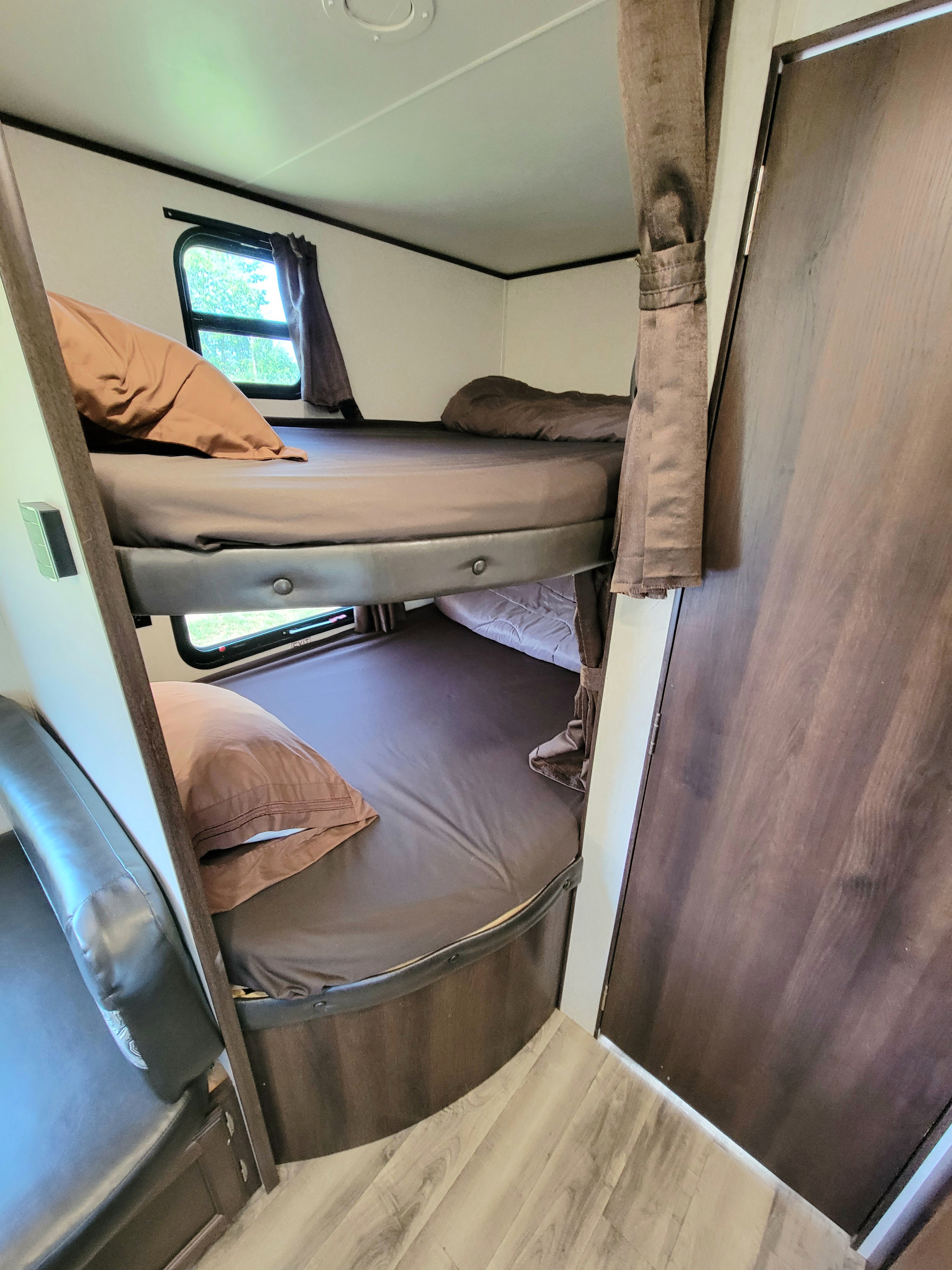 Interior of an RV rental: stacked bunk beds with brown bedding, a window, and a door. Ideal for family trips.. Jayco Jay Flight 2018