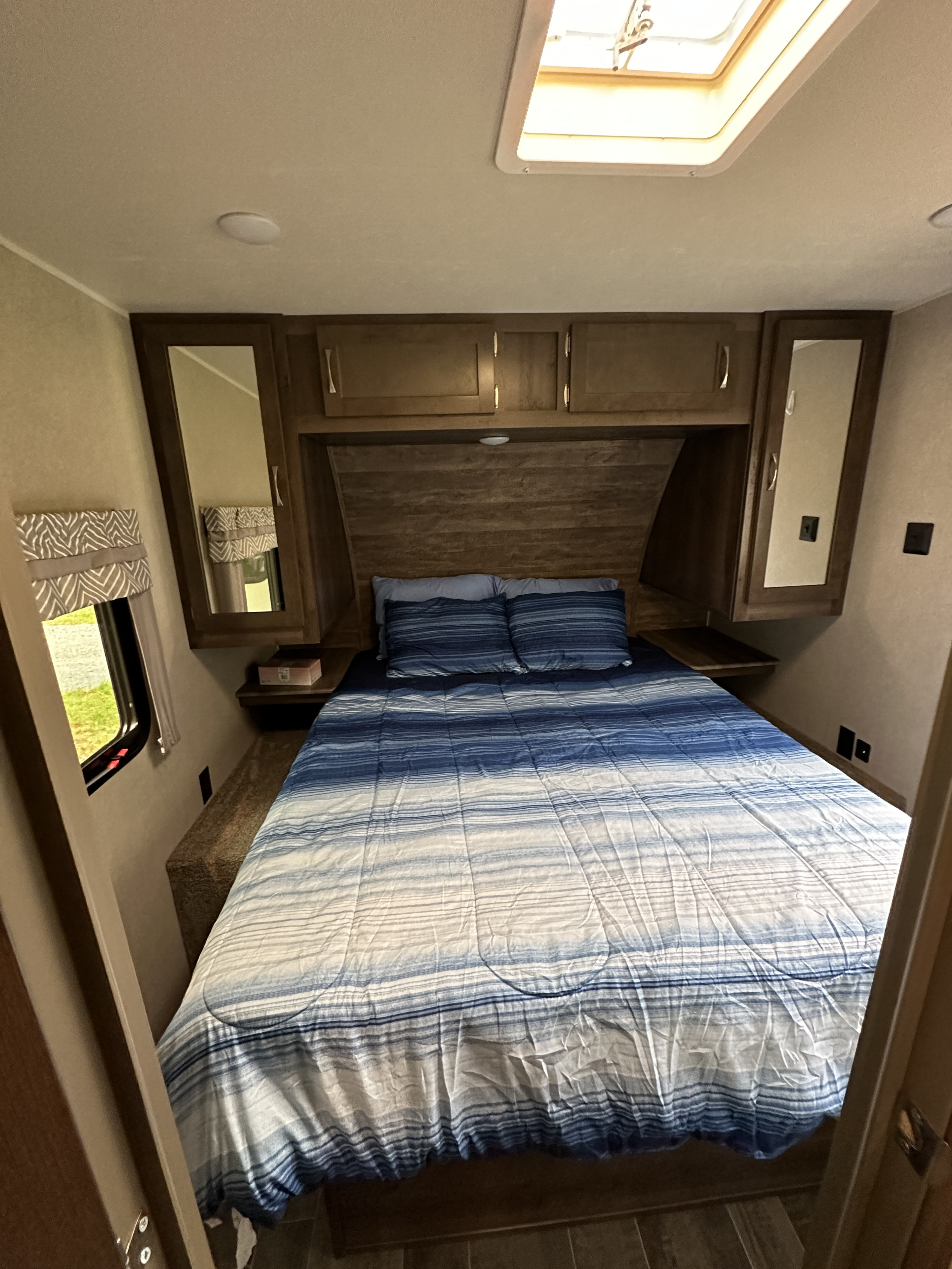 Experience comfort in this RV rental bedroom featuring a blue striped bed, overhead storage, and natural light from a skylight.. Palomino Puma 2019