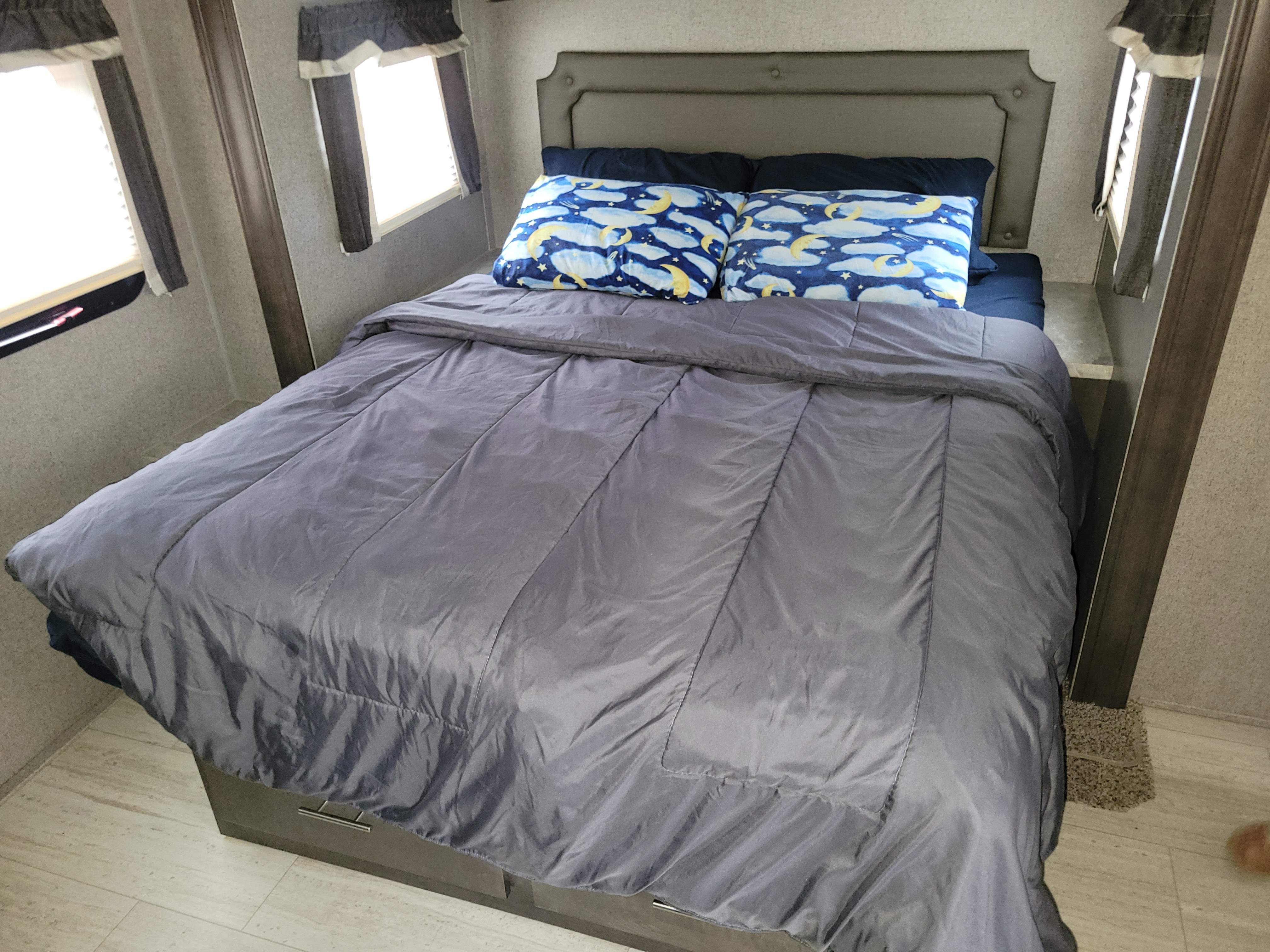 Comfortable RV rental bedroom with gray comforter, celestial pattern pillows, and side windows for a restful sleep.. Forest River Rockwood Ultra Lite 2020