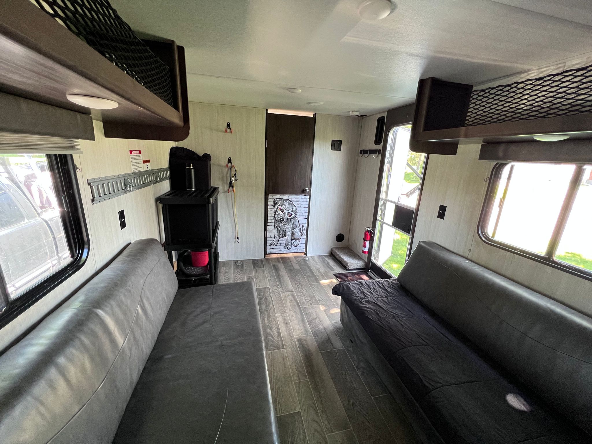 Inside an RV rental, showing a functional living space with two sofas, an overhead bunk, and wall-mounted storage tracks.. Forest River Cherokee Grey Wolf 2019