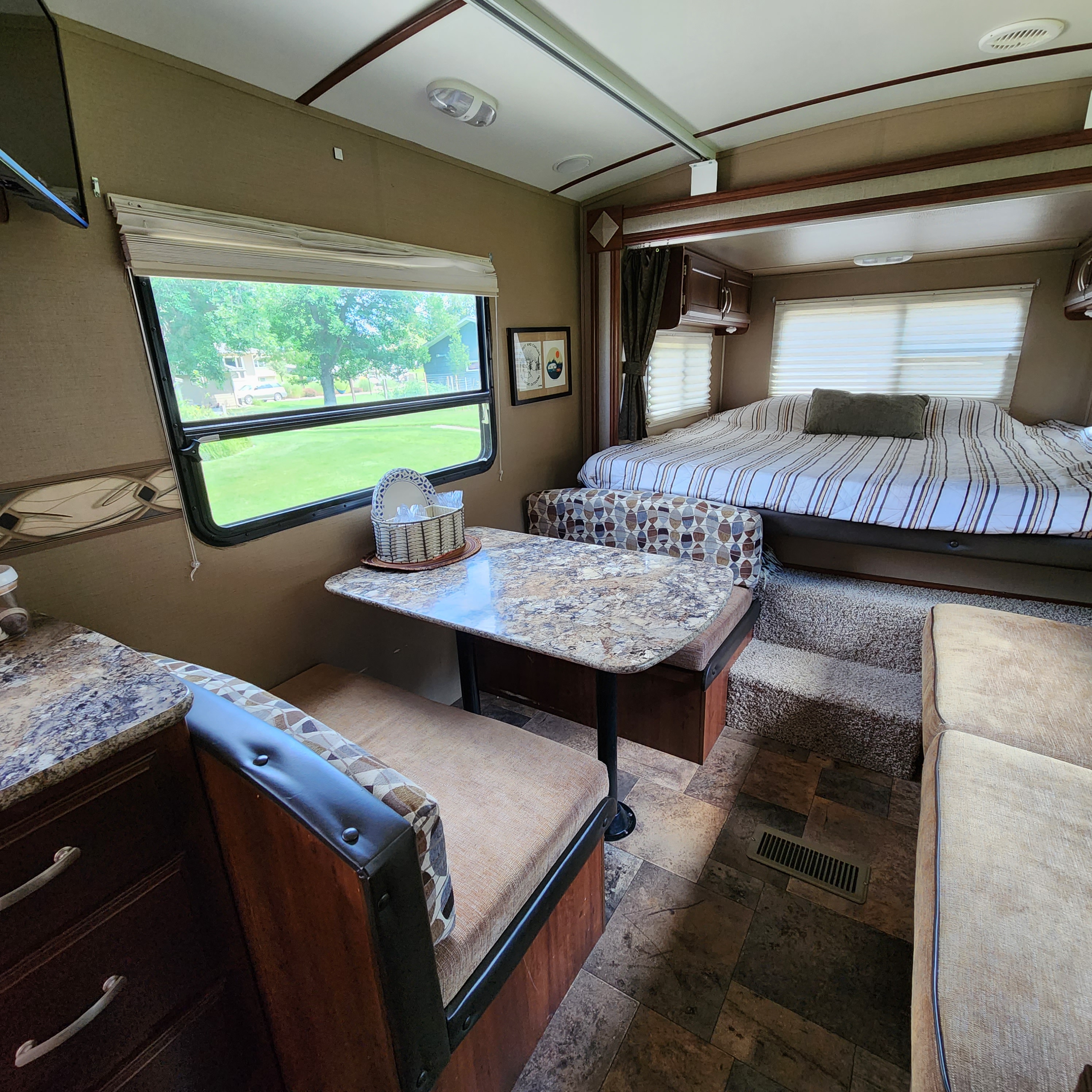 Cozy RV rental interior showing a dinette, kitchen counter, and comfortable bedroom area with a large bed.. Keystone RV Outback Terrain 2014