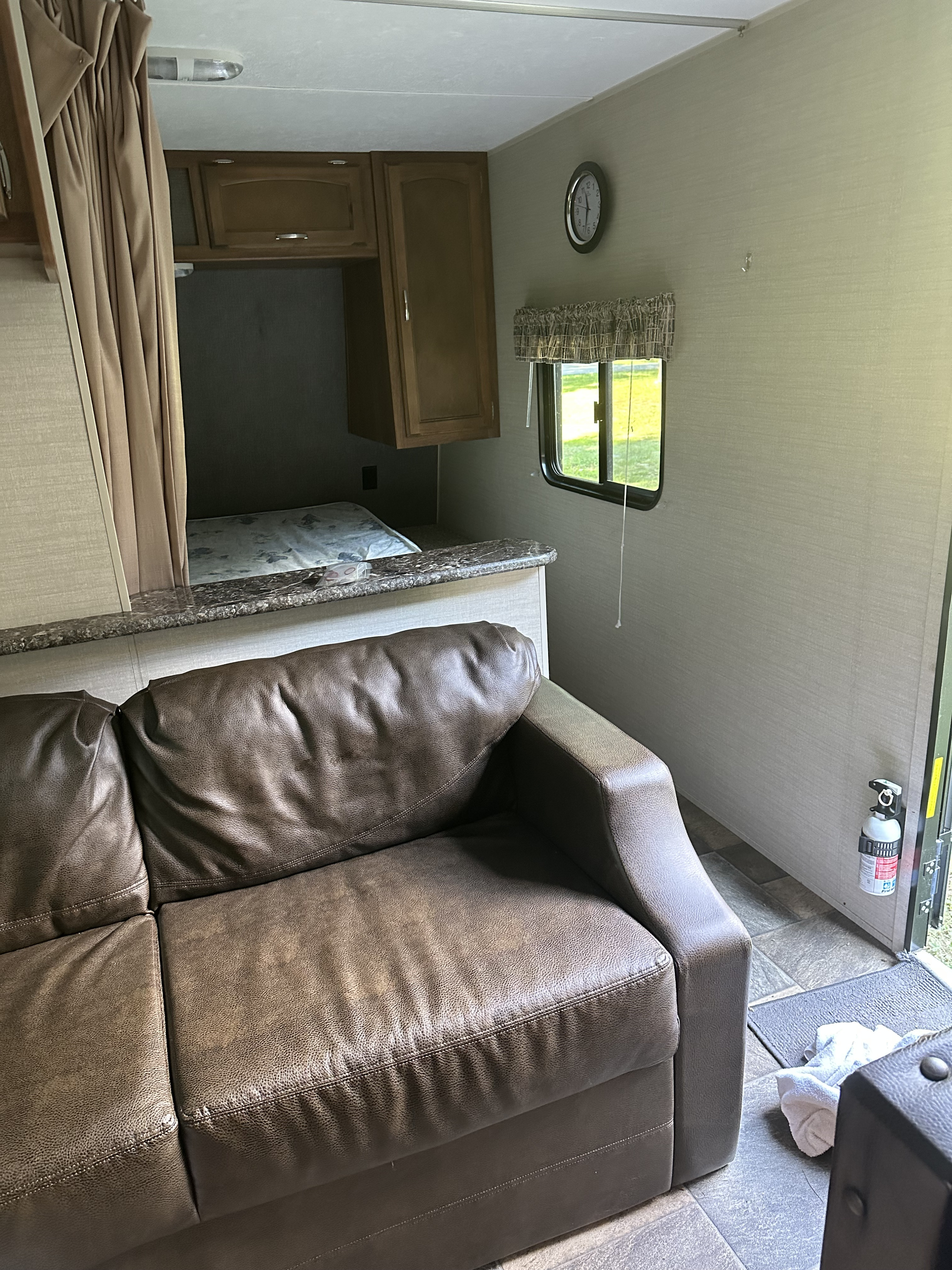 Interior of an RV rental featuring a brown leather sofa, bed area, overhead cabinets, and a mounted fire extinguisher.. Keystone RV Springdale 2016
