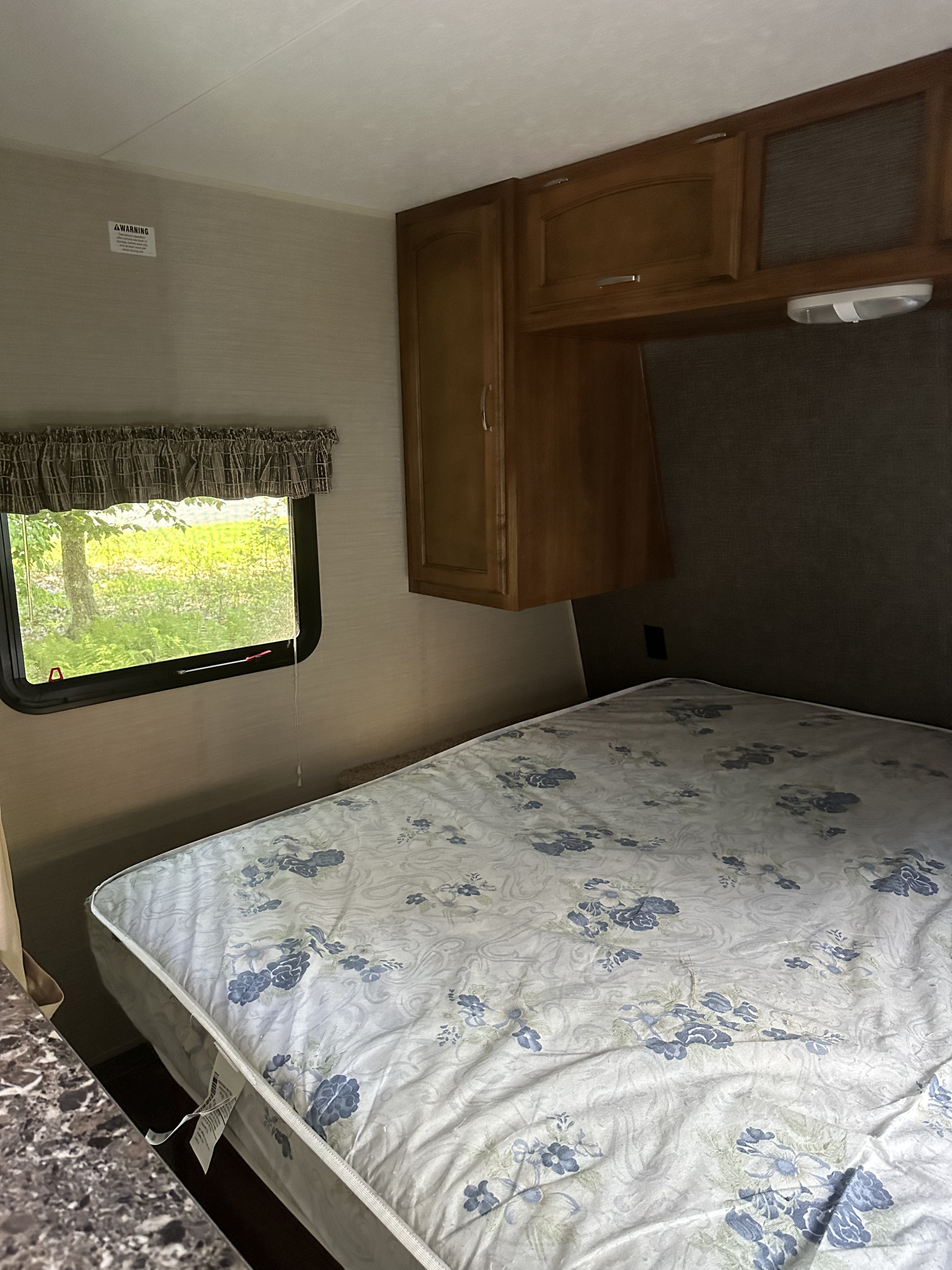 RV rental bedroom showing a bed with a floral mattress, overhead storage cabinets, and a large window.. Keystone RV Springdale 2016