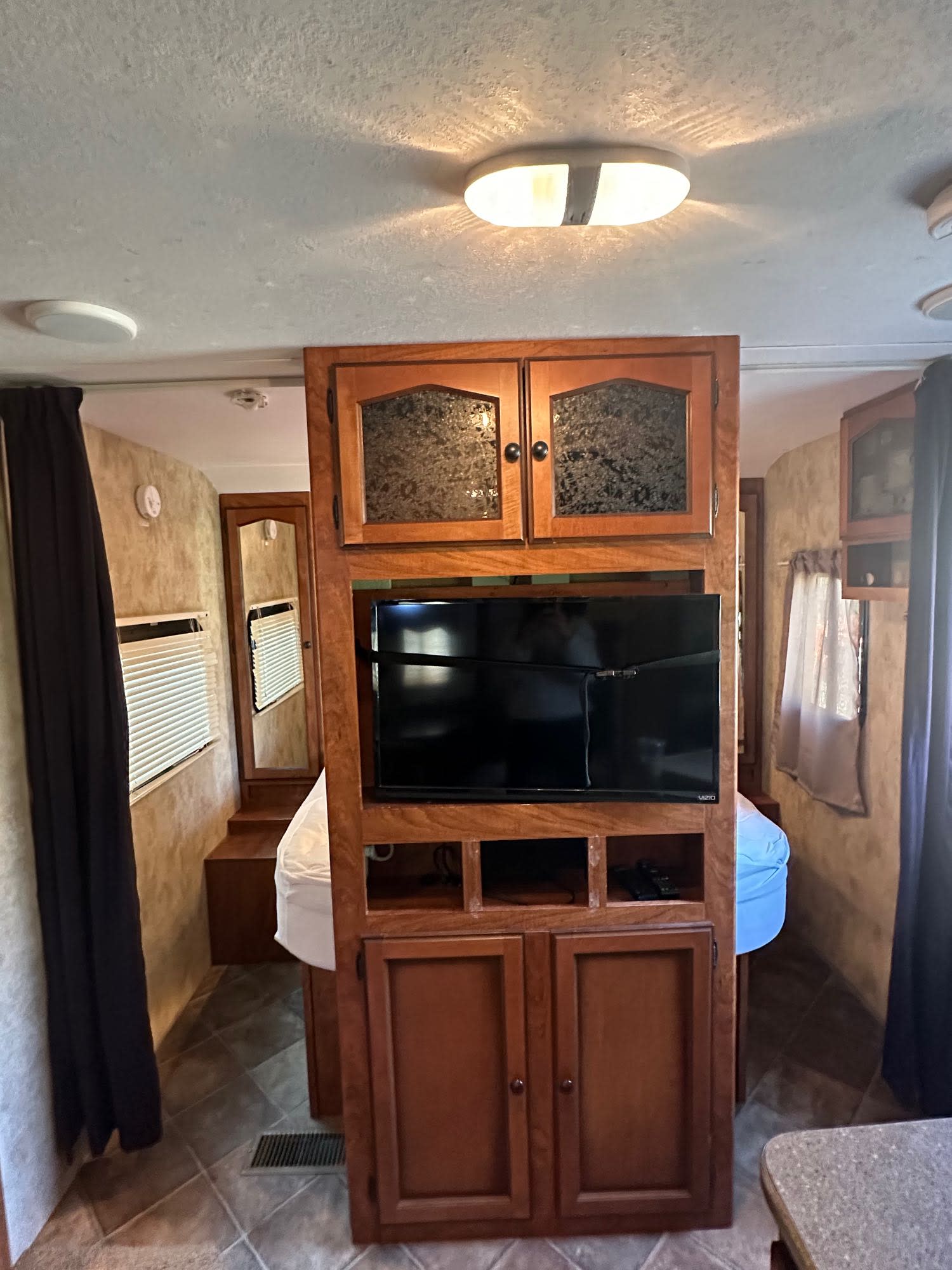 Spacious RV rental interior with central TV/cabinet dividing bedroom and living areas, featuring wood finishes.. Keystone RV Passport Ultra Lite 2012