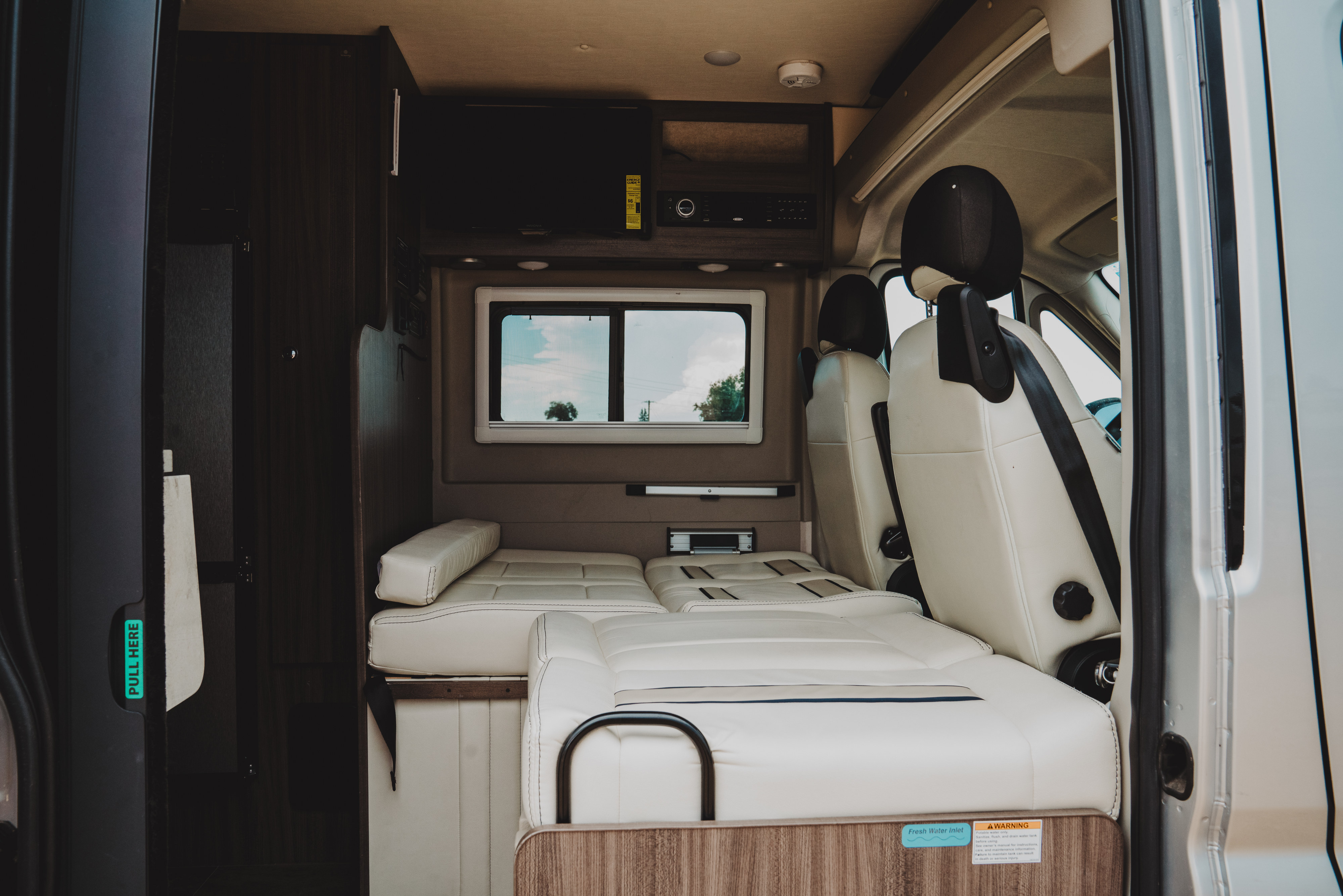Bright rv rental interior with plush cream seating/bed, TV, control panel, and swiveled front seats for comfortable camper travel.. Winnebago Travato 2019