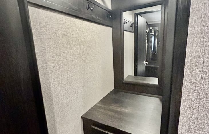 Inside your RV rental: a practical entryway with dark wood trim, coat hooks, mirror, and counter space for convenience.. Jayco White Hawk 2021