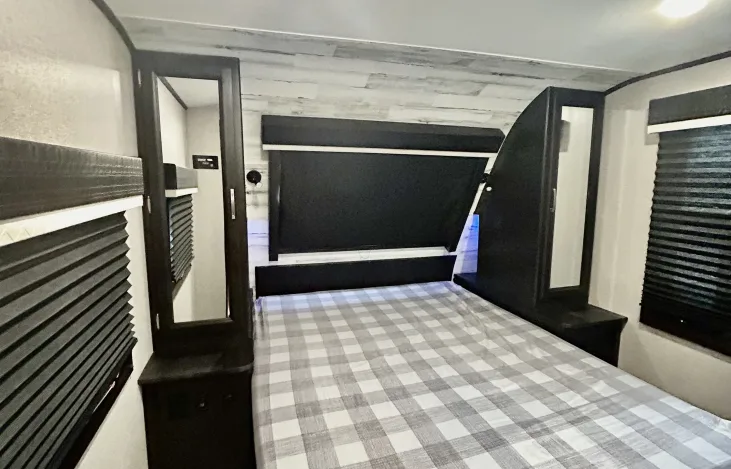 Inside an RV rental: a cozy bedroom with a plaid bed, sleek black headboard, and mirrored cabinets.. Jayco White Hawk 2021