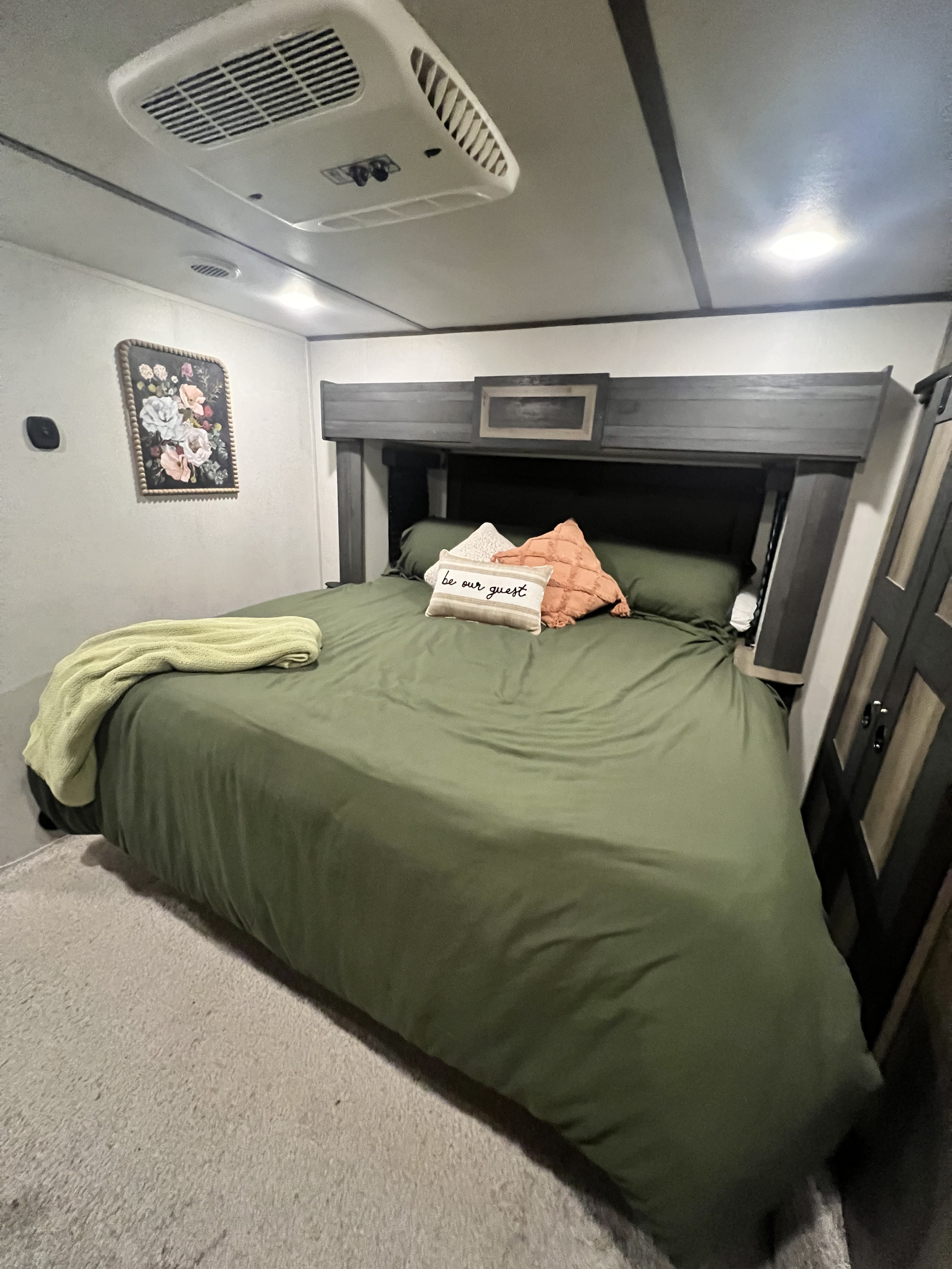 Cozy RV rental bedroom featuring an olive green bed, decorative pillows, floral wall art, and an overhead AC unit.. Keystone RV Sprinter Limited 2020