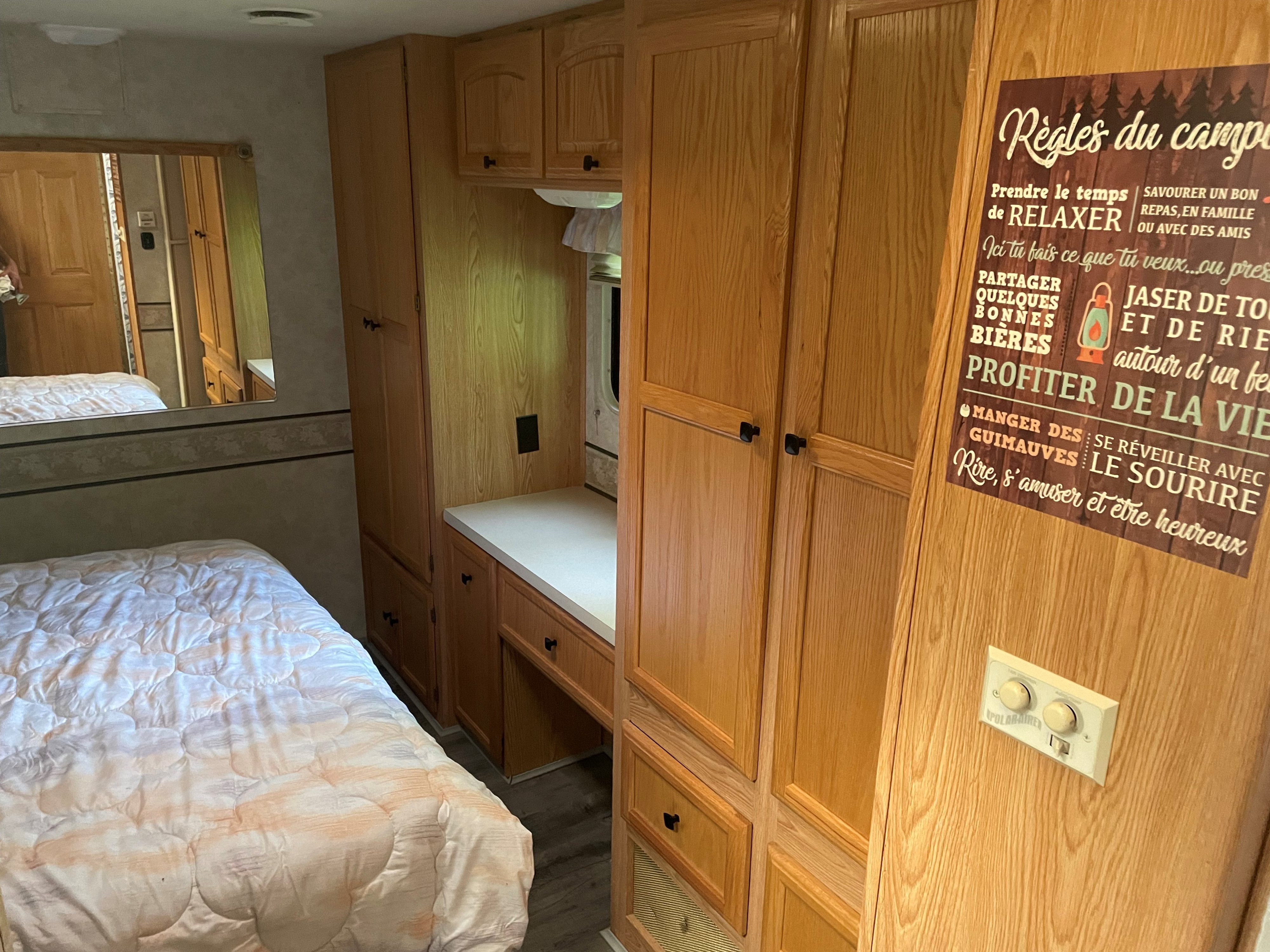 RV rental interior features a bed, wooden cabinetry, an overhead mirror, and a French "Camping Rules" sign.. Georgie Boy Pursuit 2001