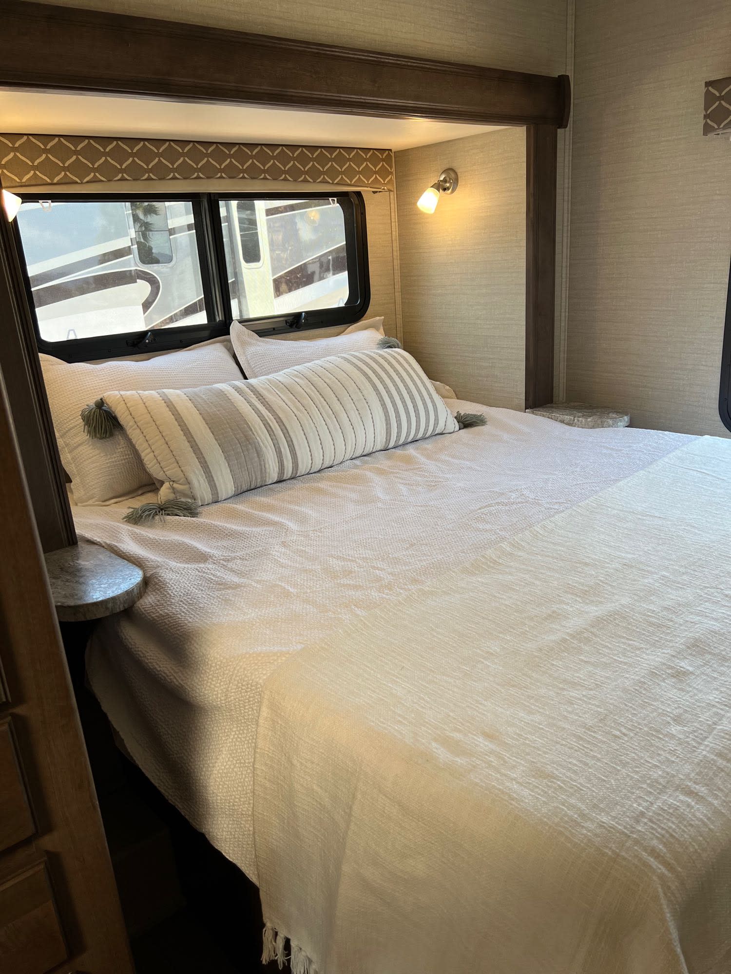 Inside an RV rental: a bright, cozy bedroom with a bed, light bedding, and windows showing another RV outside.. Jayco Greyhawk 2018
