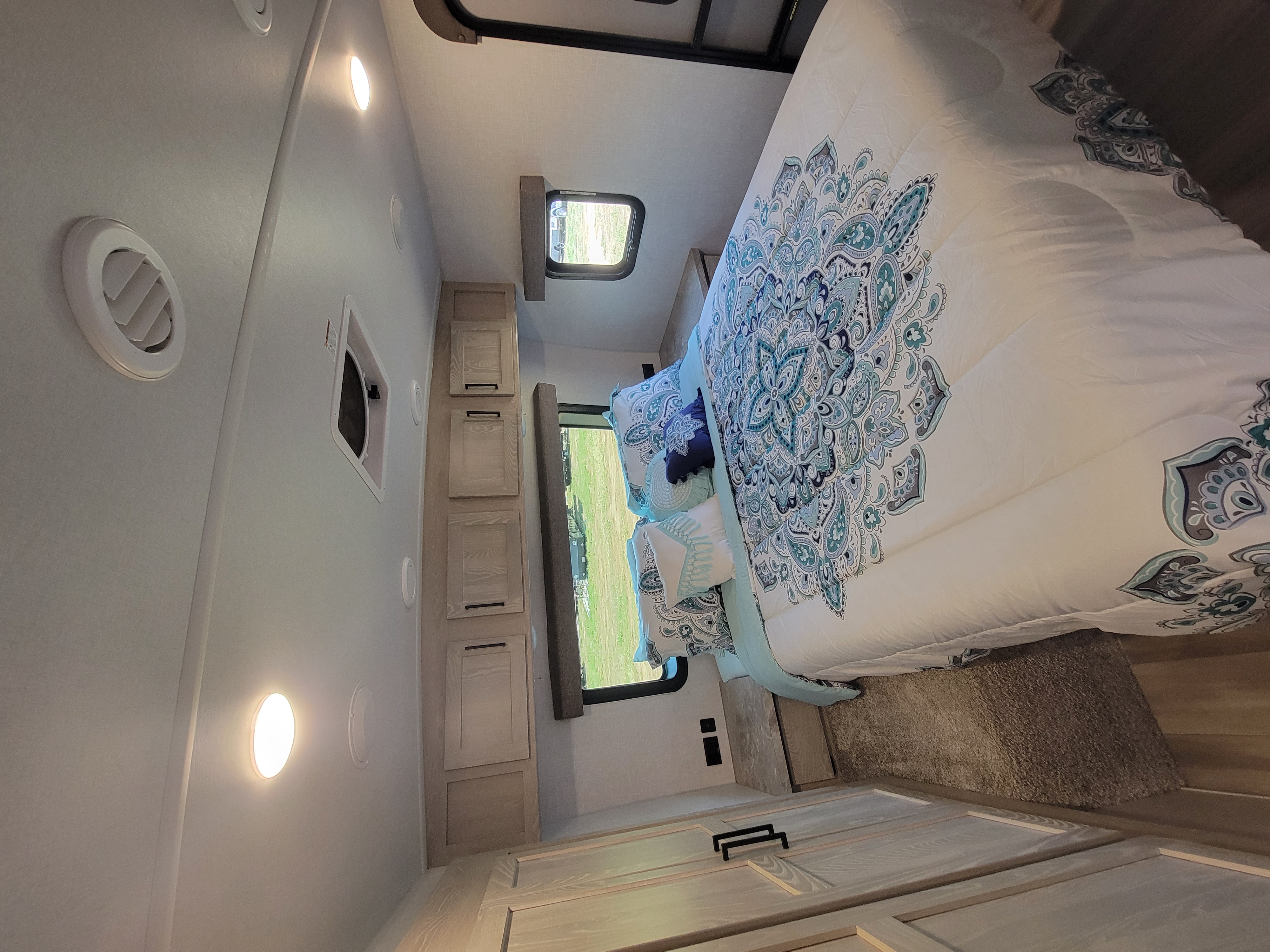 RV rental bedroom with a blue patterned comforter, light wood cabinets, and windows. Ideal for comfortable travel.. Forest River Rockwood Ultra Lite 2021