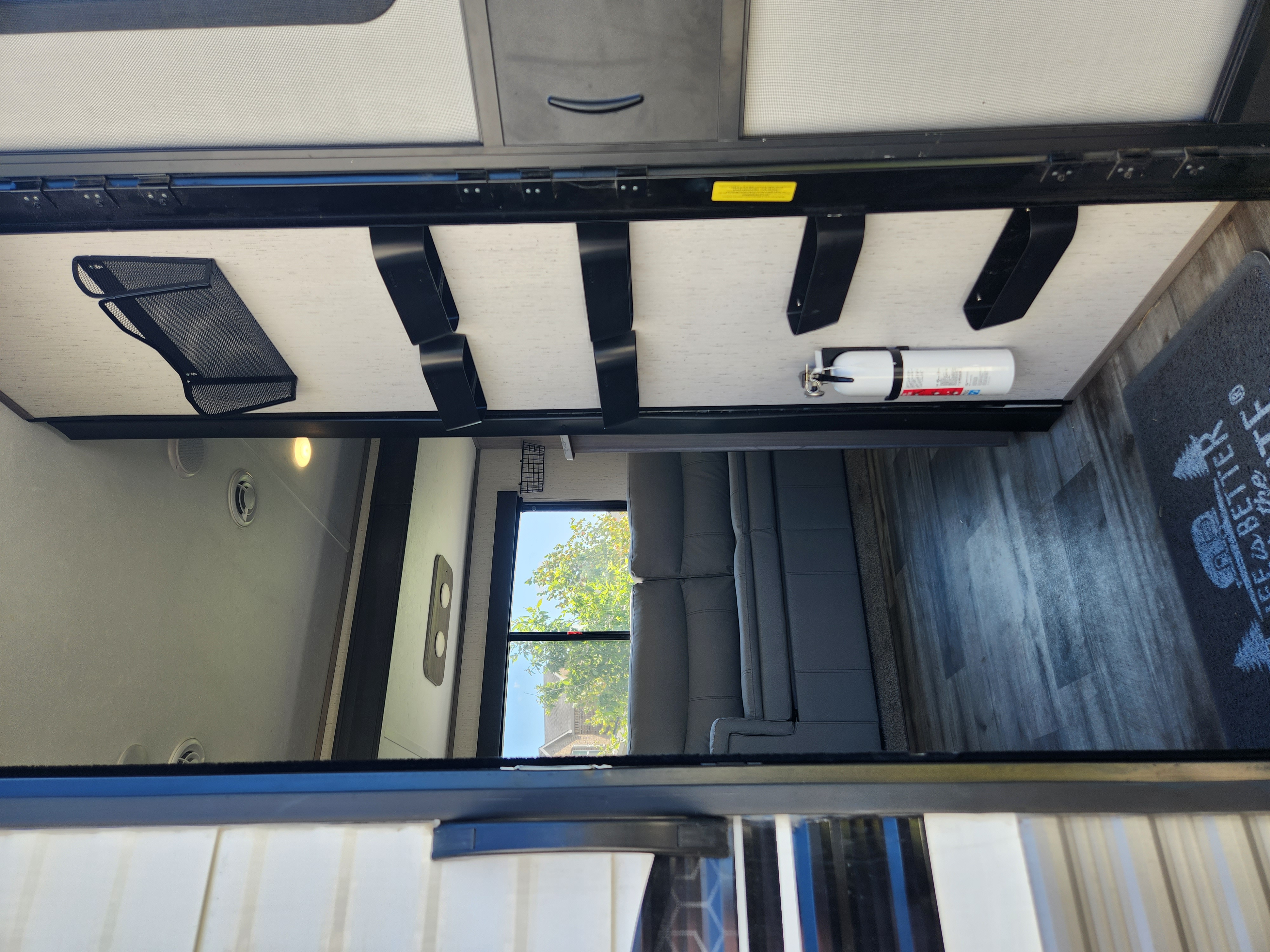 An RV rental interior with a gray sofa, wall-mounted fire extinguisher, and practical overhead storage.. Dutchmen Coleman 2022