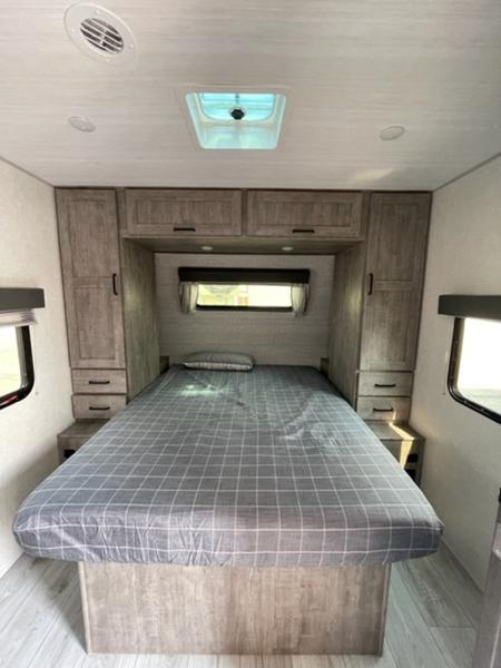 Inside an RV rental: a modern bedroom with a large bed, ample storage, skylight, and light wood finishes.. Forest River Surveyor Legend 260BHLE 2023