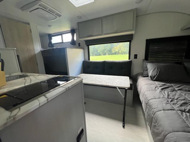 Cozy RV rental interior: well-equipped kitchen, dinette, and comfortable bed. Window shows green scenery.. Forest River Wildwood FSX 2023
