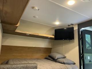 Inside an RV rental: a comfortable bed with grey bedding, a mounted TV, and warm wooden interior details.. Forest River Cherokee 2024