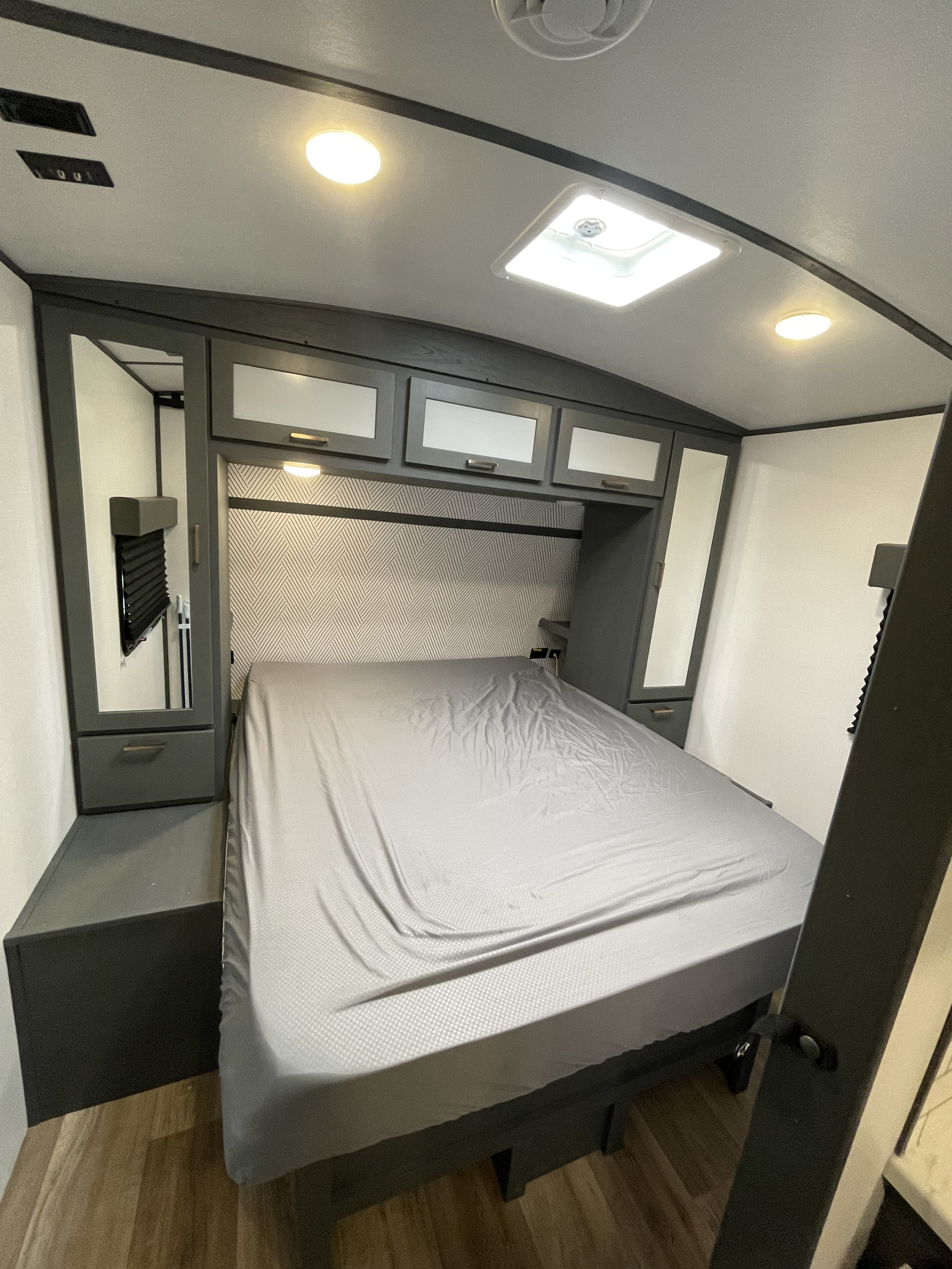Modern grey RV rental bedroom featuring a comfortable bed, integrated storage, and bright overhead lights.. Keystone RV Bullet Ultra Lite 2023