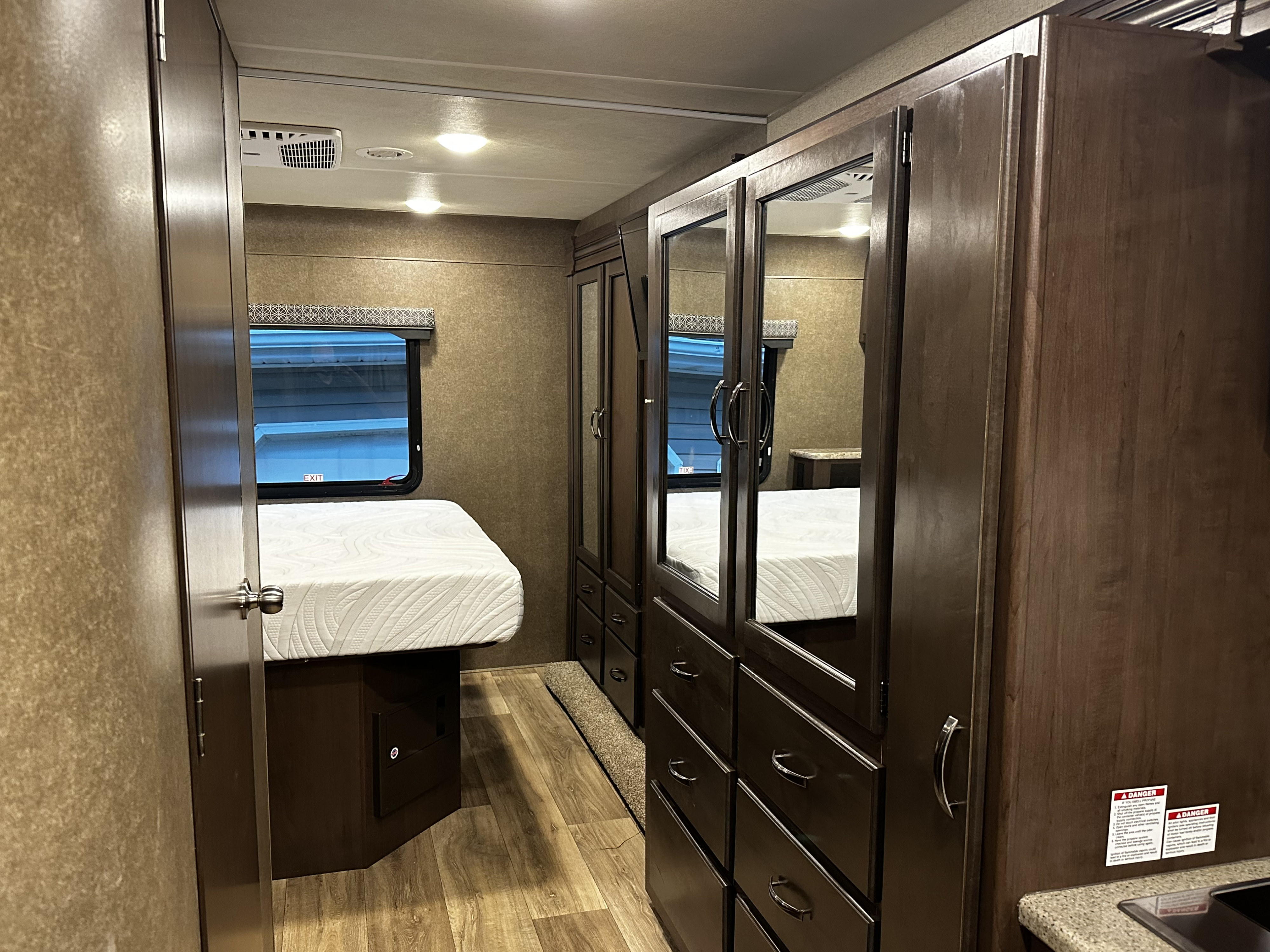 RV rental bedroom interior featuring a comfortable bed, window with exit, and spacious mirrored dresser/wardrobe.. Thor Four Winds 2019
