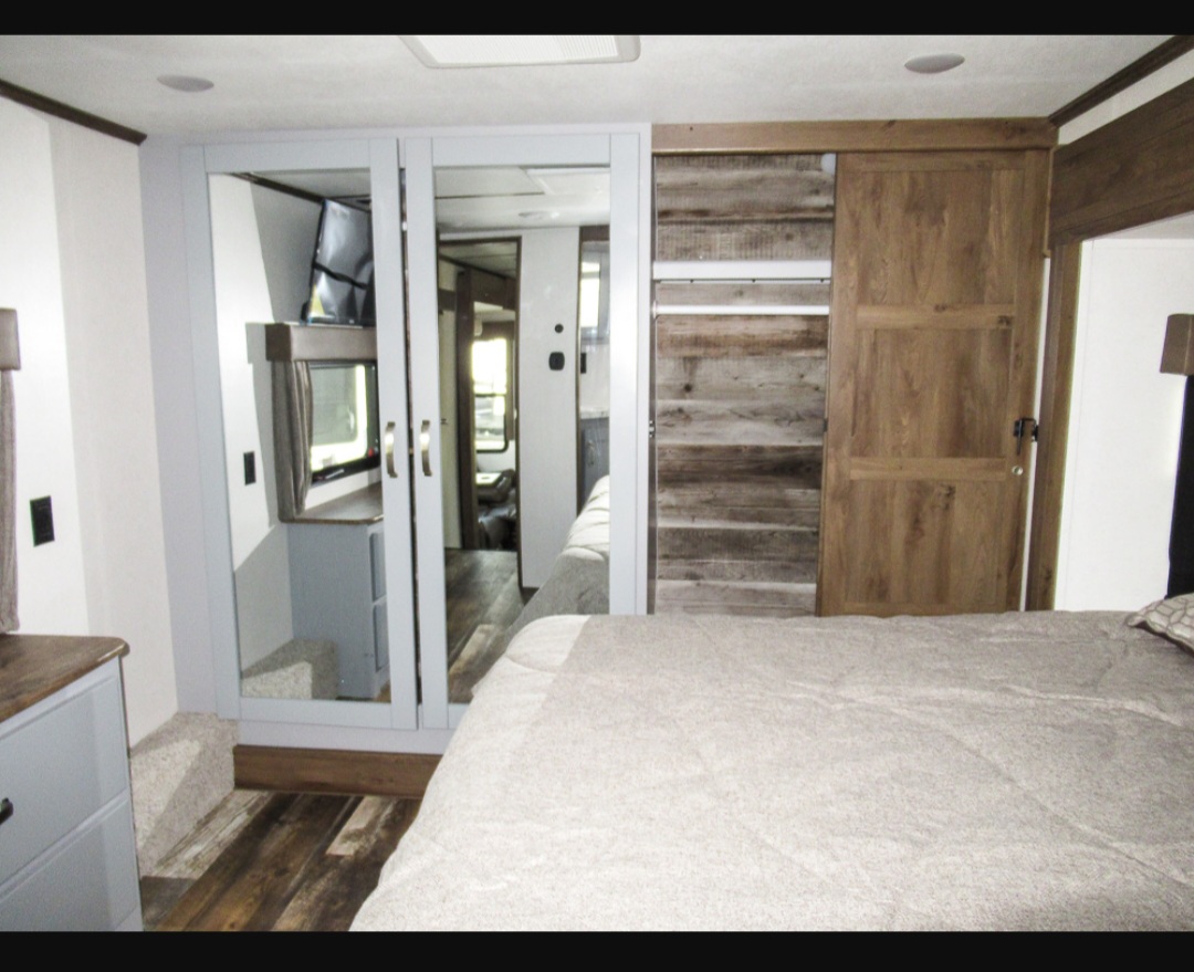 Modern RV rental bedroom featuring mirrored closet doors, rustic wood accents, and a large bed.. Keystone RV Fuzion Toy Hauler 2021