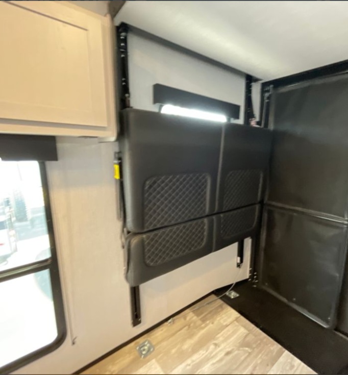 RV rental interior: foldable wall-mounted bunk/sofa with padded sections in a versatile toy hauler space.. Heartland RVs Fuel Toy Hauler 2022