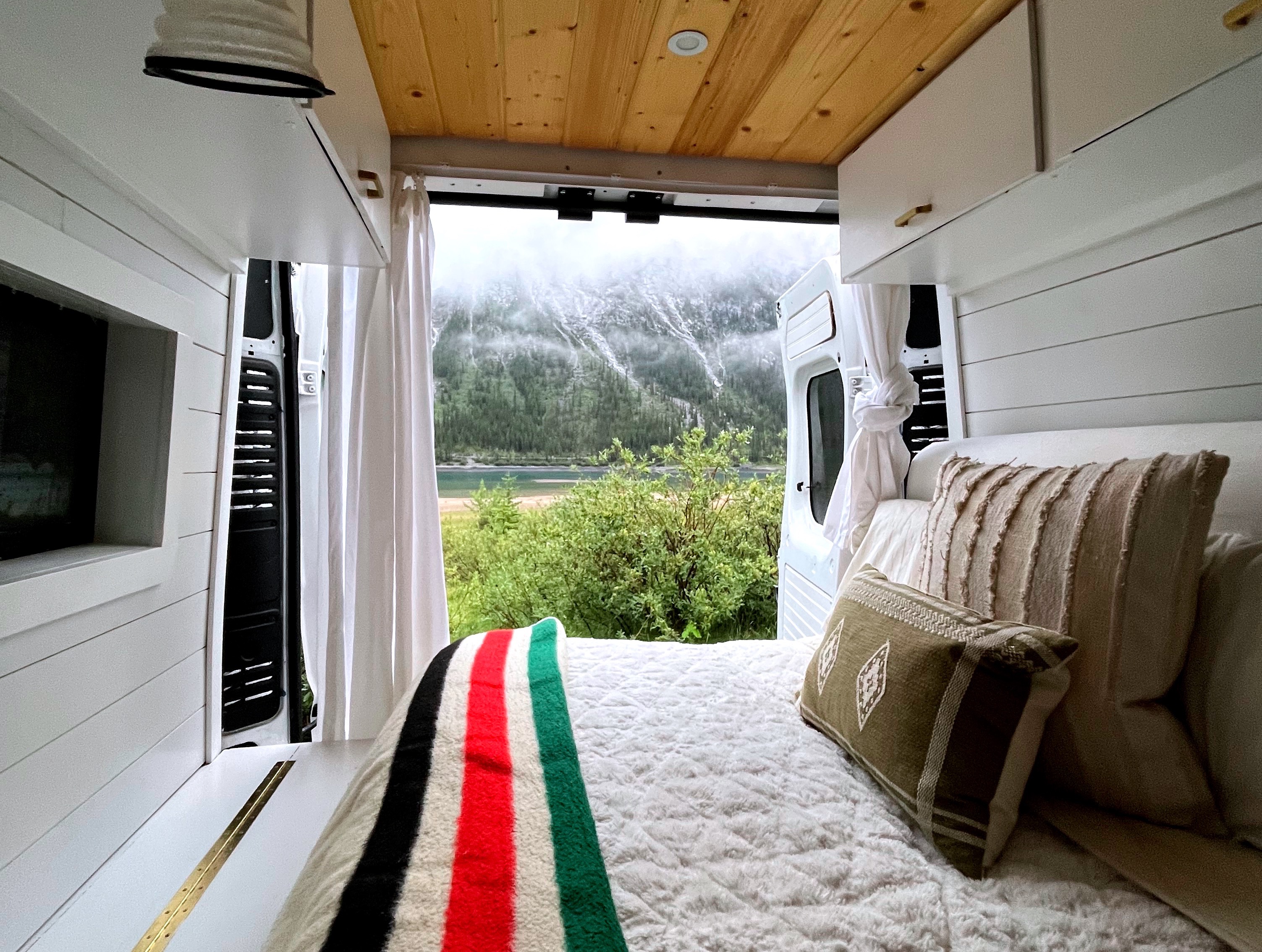 Cozy rv rental interior with open back doors showcasing a stunning mountain and lake view. Perfect for outdoor adventures!. Dodge Sprinter 2014