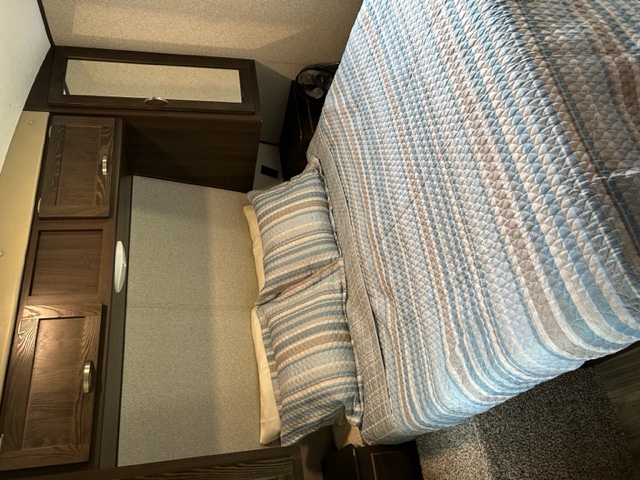 Cozy RV rental bedroom featuring striped bedding, dark wood cabinets, a wall mirror, and ample storage for travelers.. Keystone RV Springdale 2018