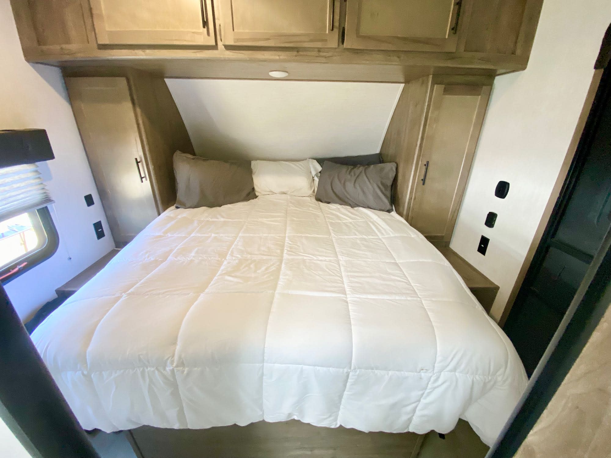 RV rental bedroom with a cozy bed, overhead cabinets, and side storage on both sides of the bed.. Forest River Vengeance 2021